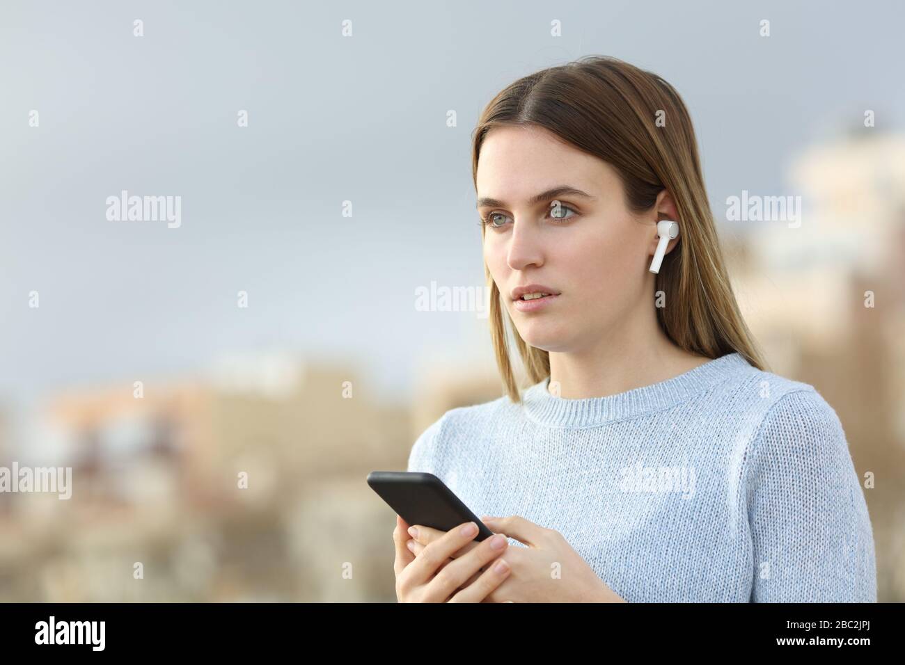 Serious girl looking away listening to music with earphones and mobile phone Stock Photo