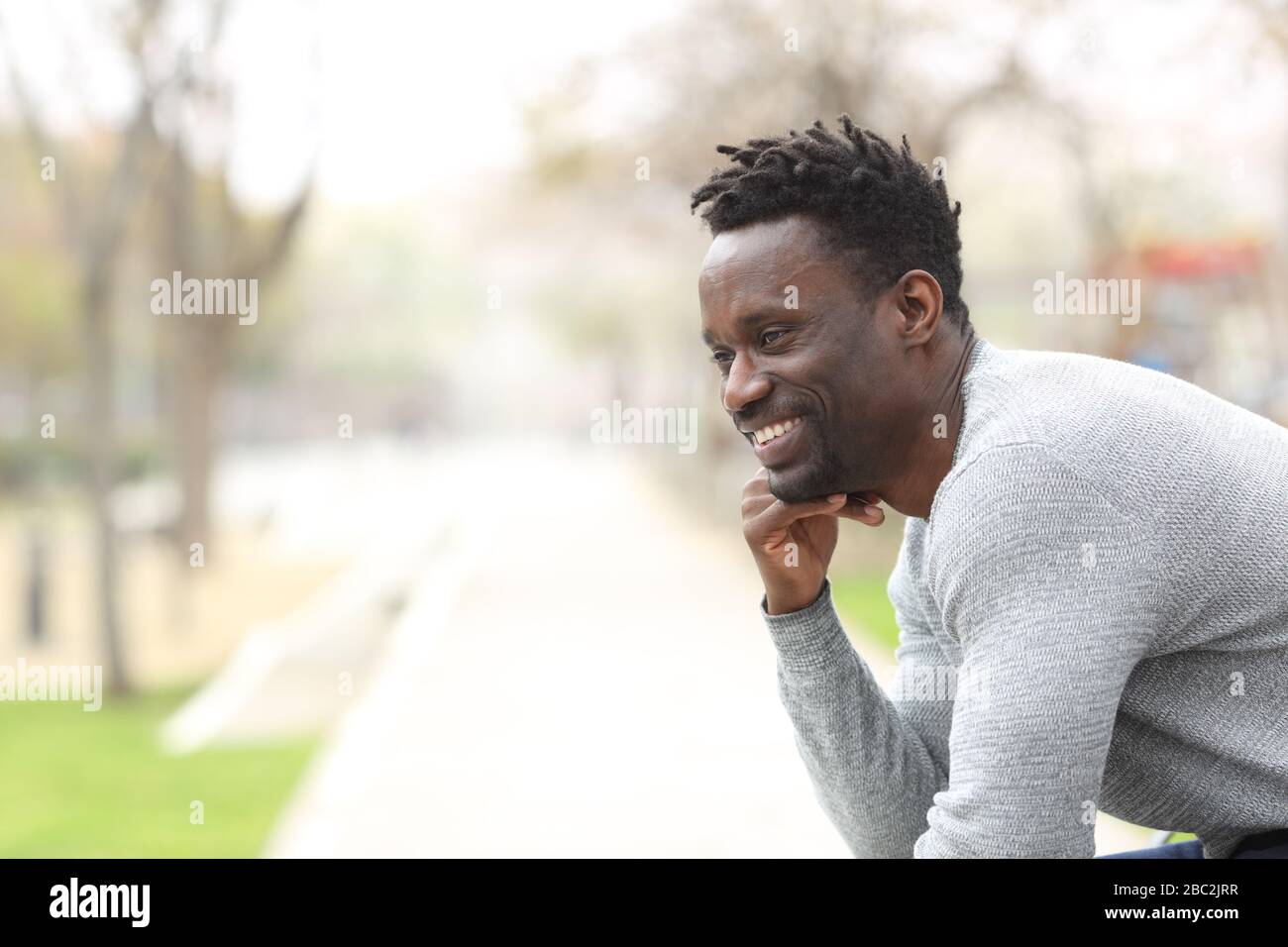 Portrait of a happy black man looking away sitting at the park bench Stock Photo