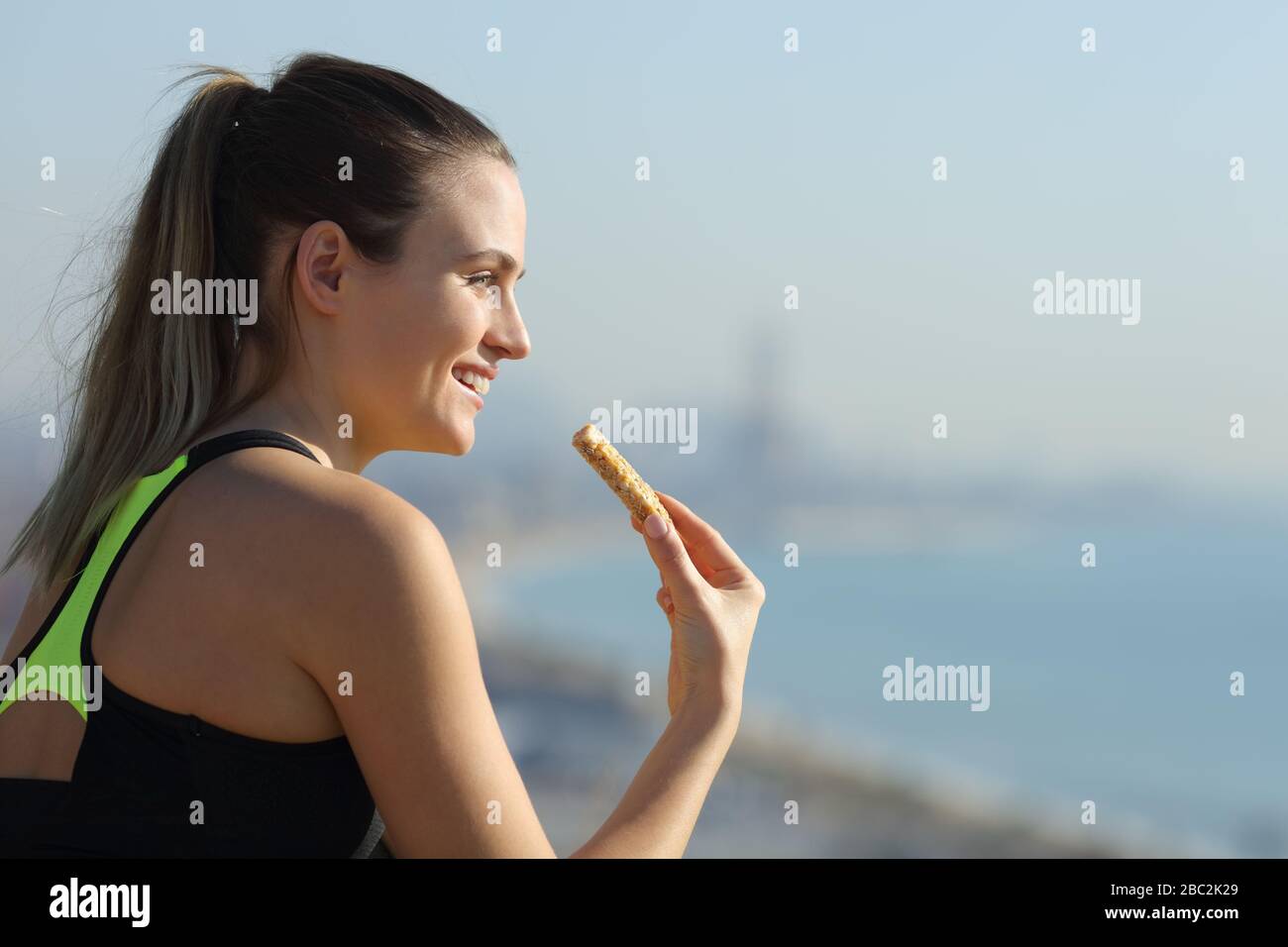 Happy runner woman eating energy bar after exercise contemplating beach views Stock Photo