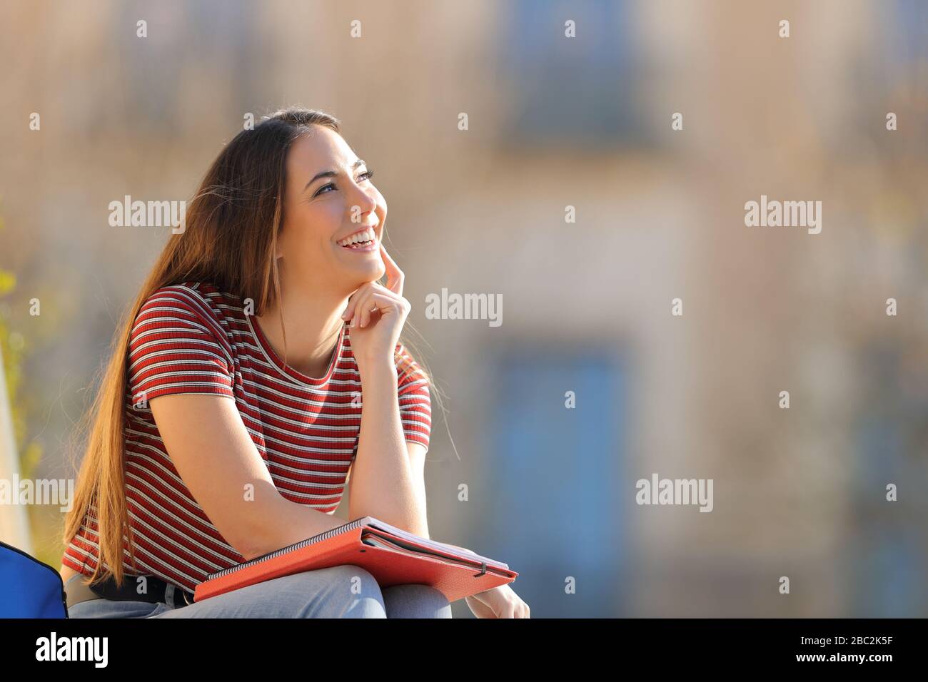 Happy student thinking looking at side sitting outdoors in a university campus Stock Photo