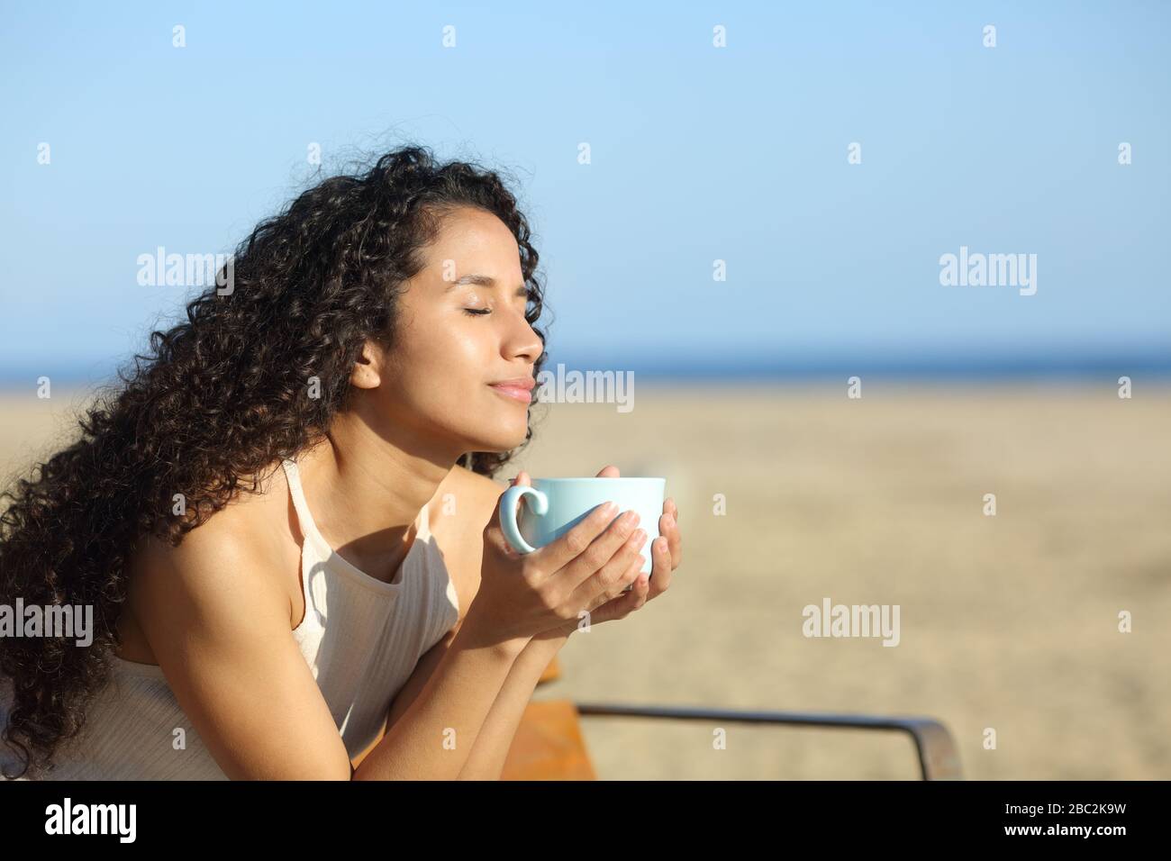 Latin woman enjoying a cup of coffee breathing fresh air on the beach a