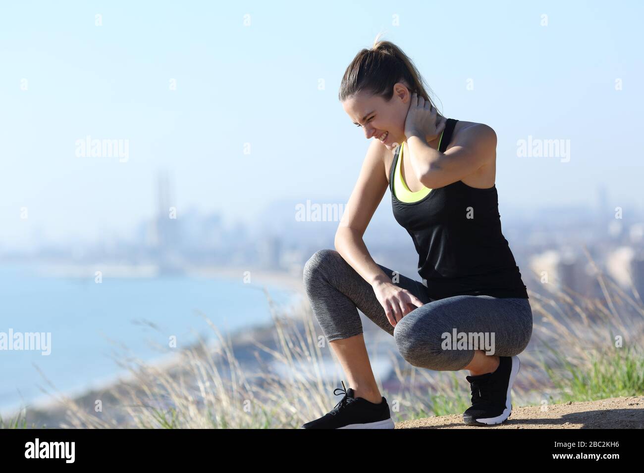 Injured runner woman suffering neck ache after sport in city outskirts Stock Photo