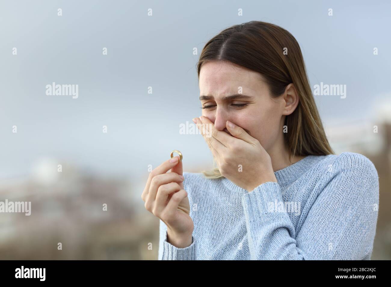 Sad divorced girl complaining crying looking at wedding ring in the street Stock Photo