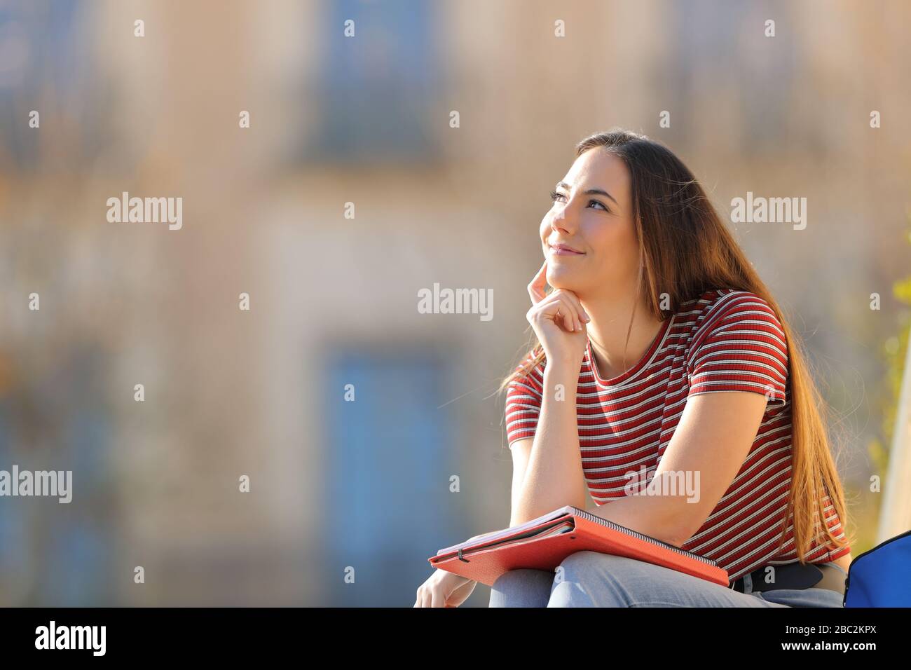 Satisfied student thinking looking at side sitting in a campus a sunny day Stock Photo