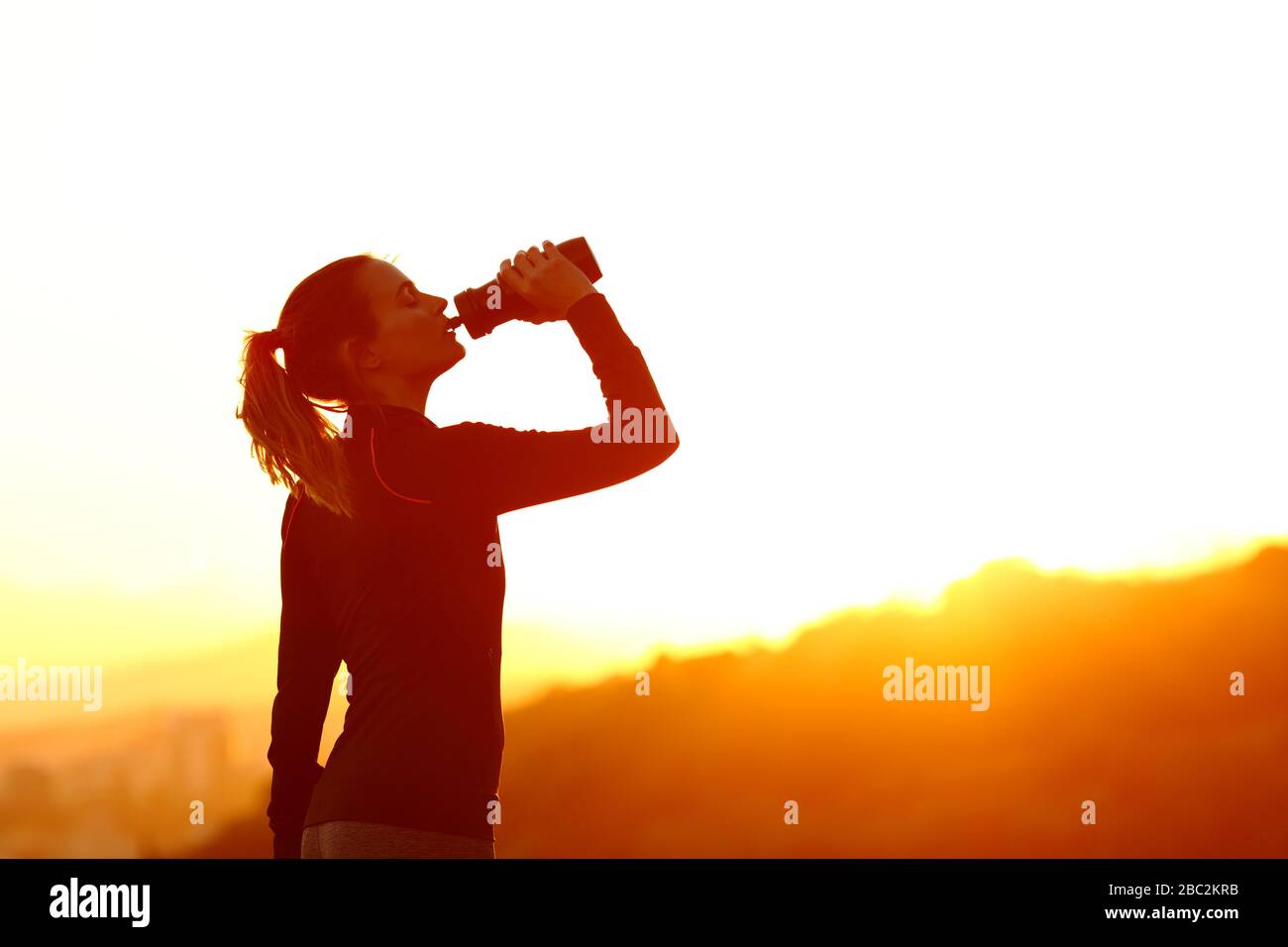 Silhouette of a runner woman drinking water from bottle at sunset Stock Photo