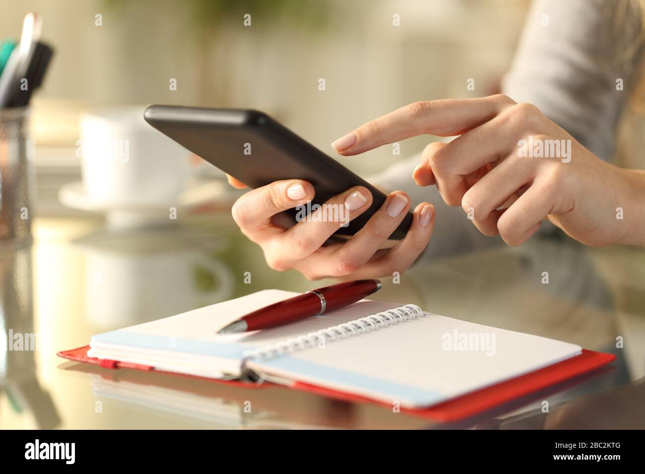 Close up of woman hands checking smart phone with personal organizer diary or agenda over the table at home Stock Photo