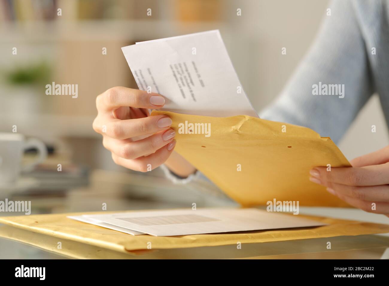 Close up of woman hands opening a letter on a padded envelope on a desk at home Stock Photo