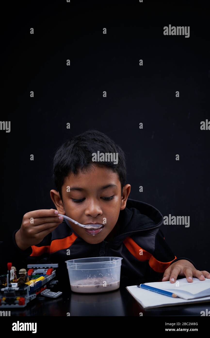 Little boy eating breakfast and doing his study at home quarantine, Coronavirus Disease Stock Photo