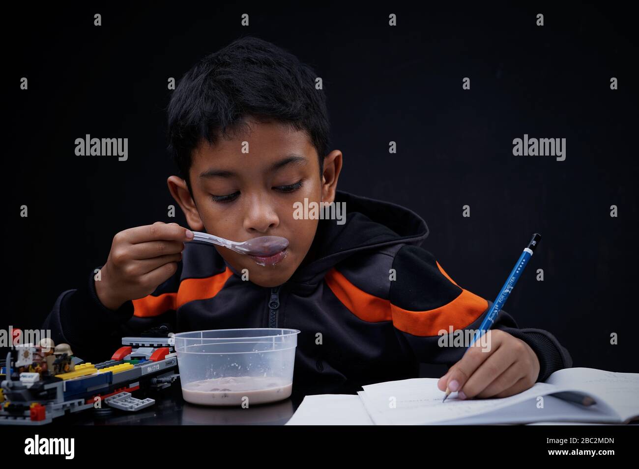 Little boy eating breakfast and doing his study at home quarantine, Coronavirus Disease Stock Photo