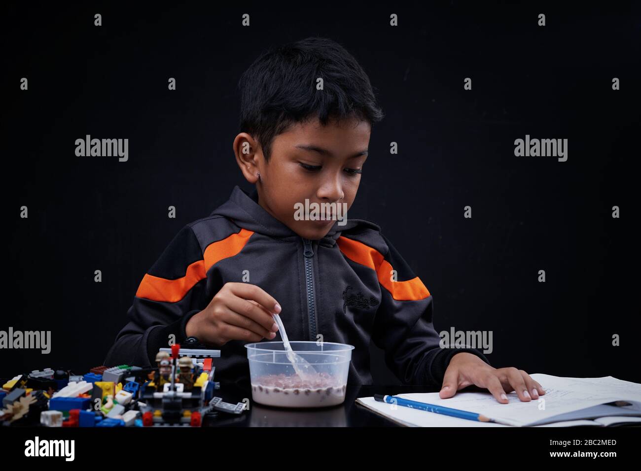 Little boy eating breakfast and doing his study at home quarantine, Coronavirus Disease Stock Photo