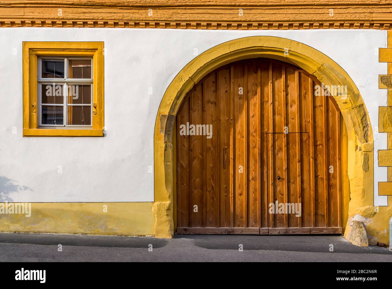 Facade of a restored half-timbered house partly plastered with window and driveway with round arch and fitted wooden gate Stock Photo