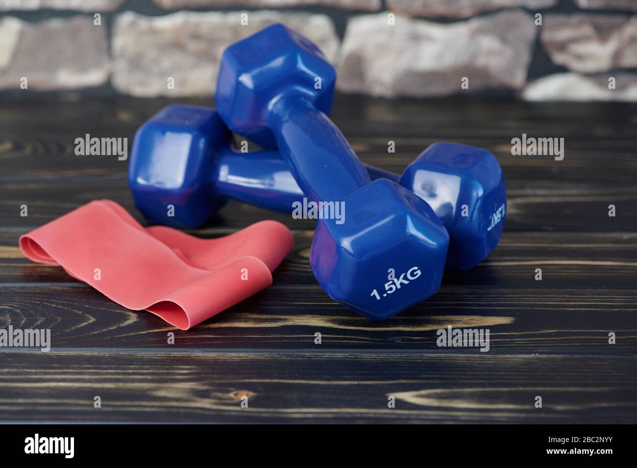 red elastic exercise band beside blue dumbbells on wooden surface Stock Photo