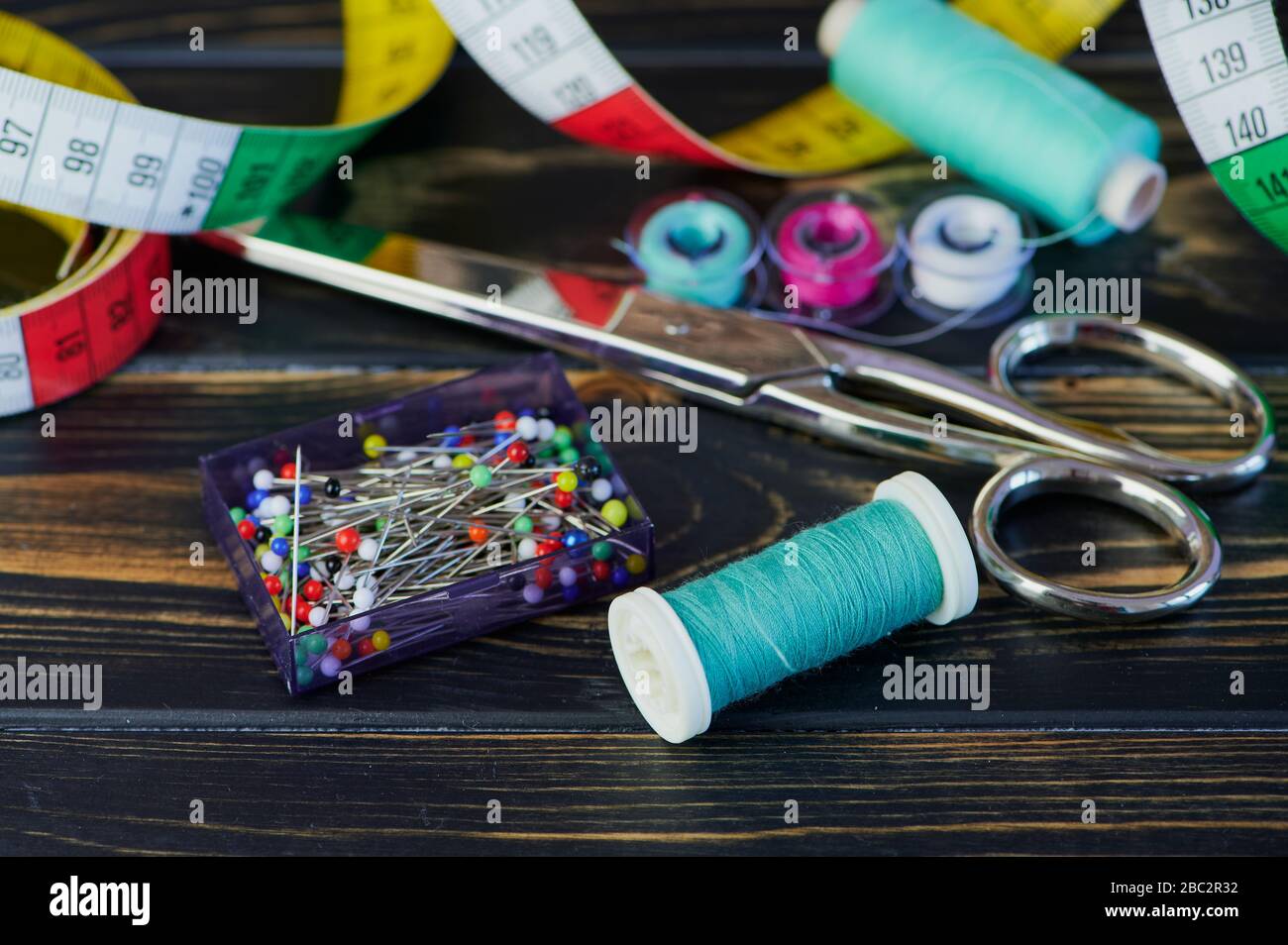 macro color photo of different sewing tools like scissors and sewing thread on wooden table Stock Photo