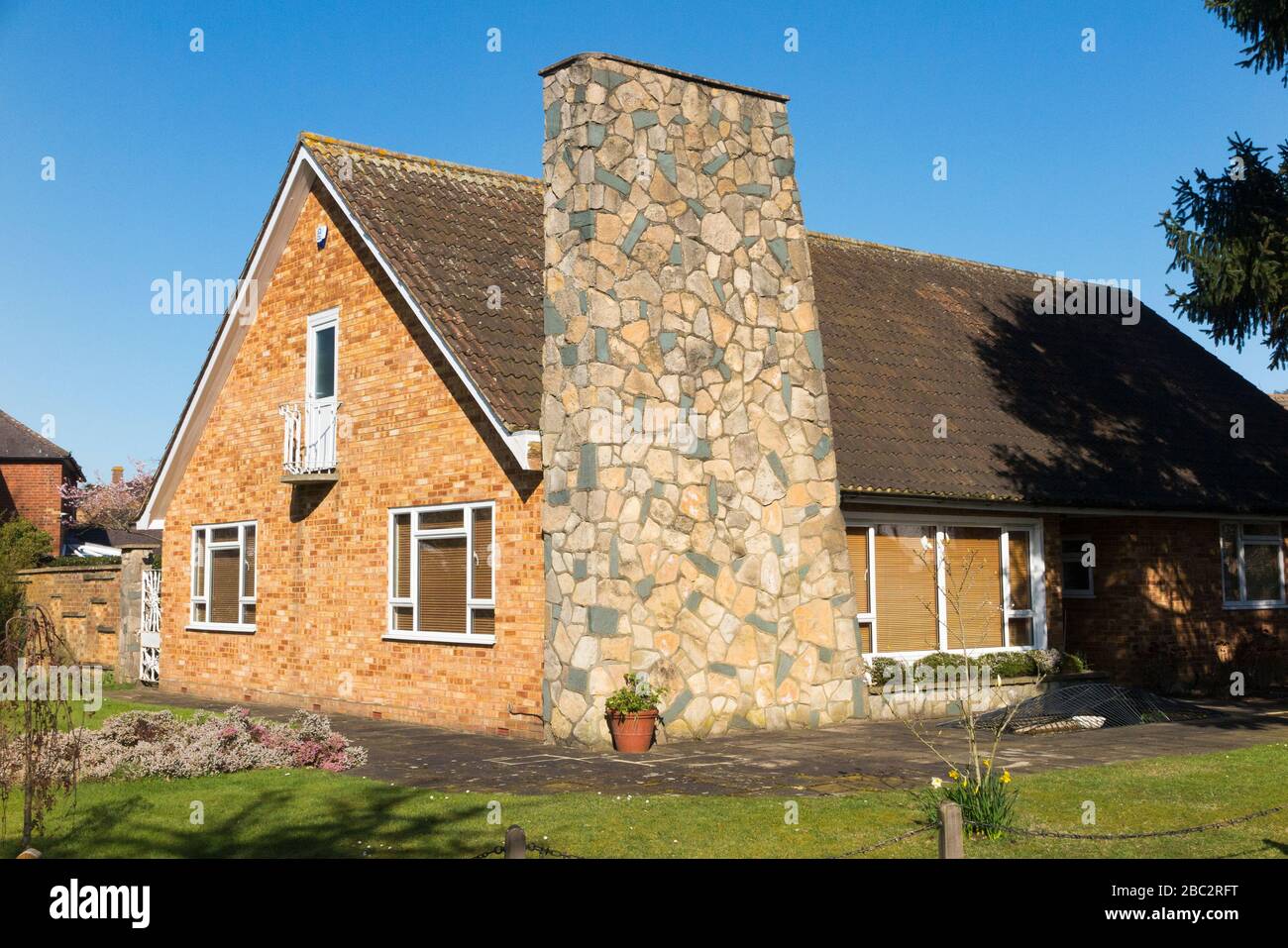 Chalet style brick bungalow with 1960s or 1970s architecture and a large pronounced feature chimney made from stone. Surrey, UK. (116) Stock Photo