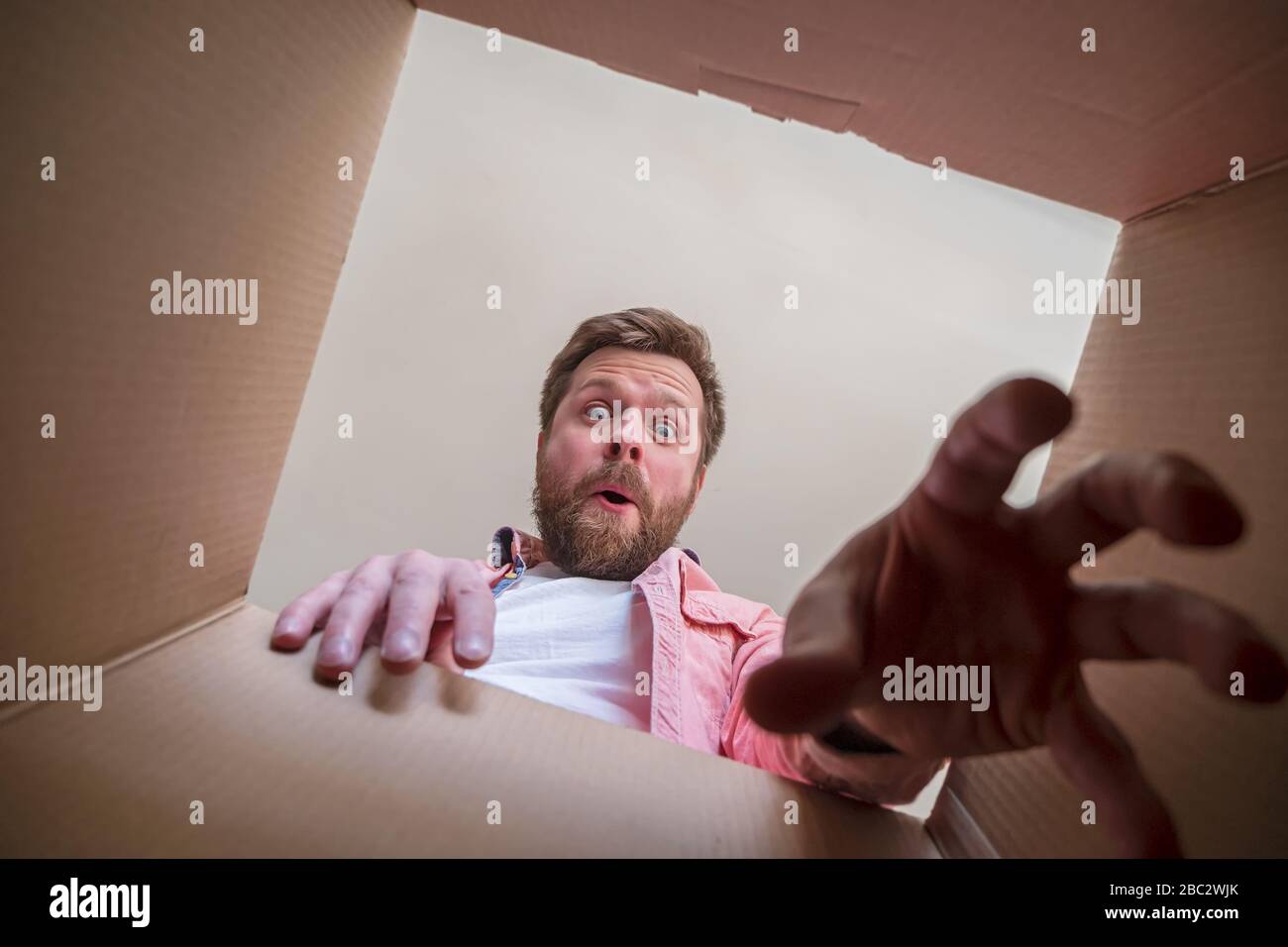 Surprised, a happy man holds out his hand trying to get a gift or parcel from an unpacked box. Unboxing inside view. Stock Photo