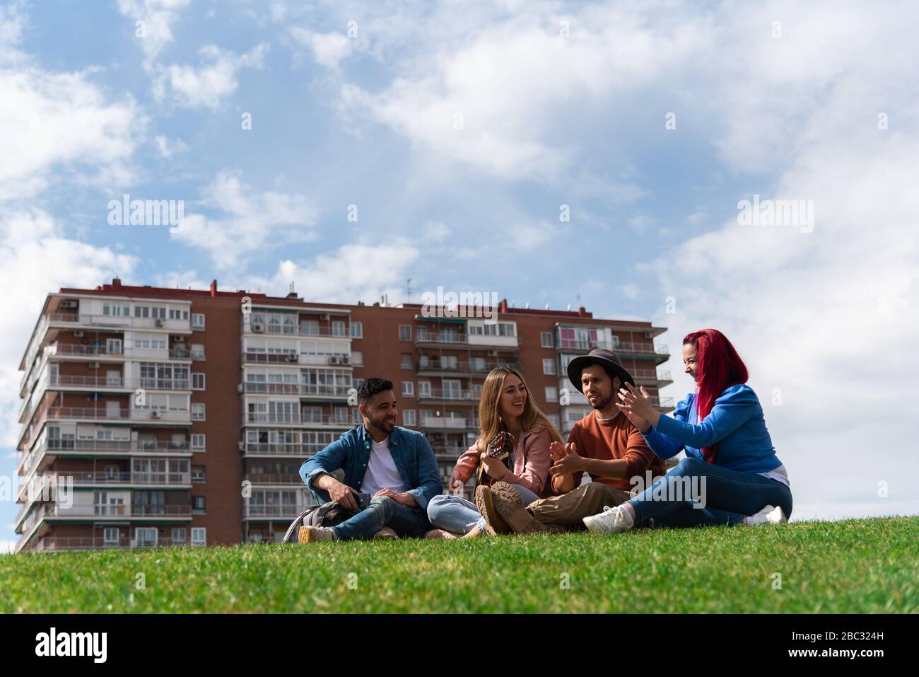 Two young Hispanic men enjoy music with a guitar next to two Caucasian girls in a city park, image includes space for text Stock Photo