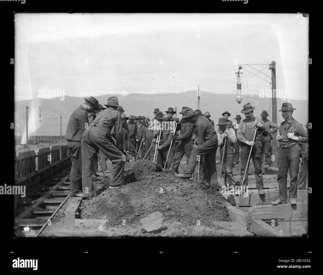 Group of laborers digging through dirt pile along railway bed Stock