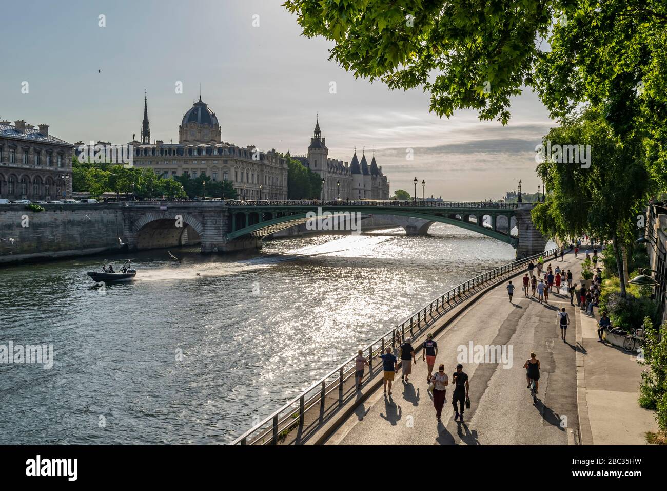 Paris view across the River Seine on sunny day, with bridge and people walking alongside the river, backlit Stock Photo