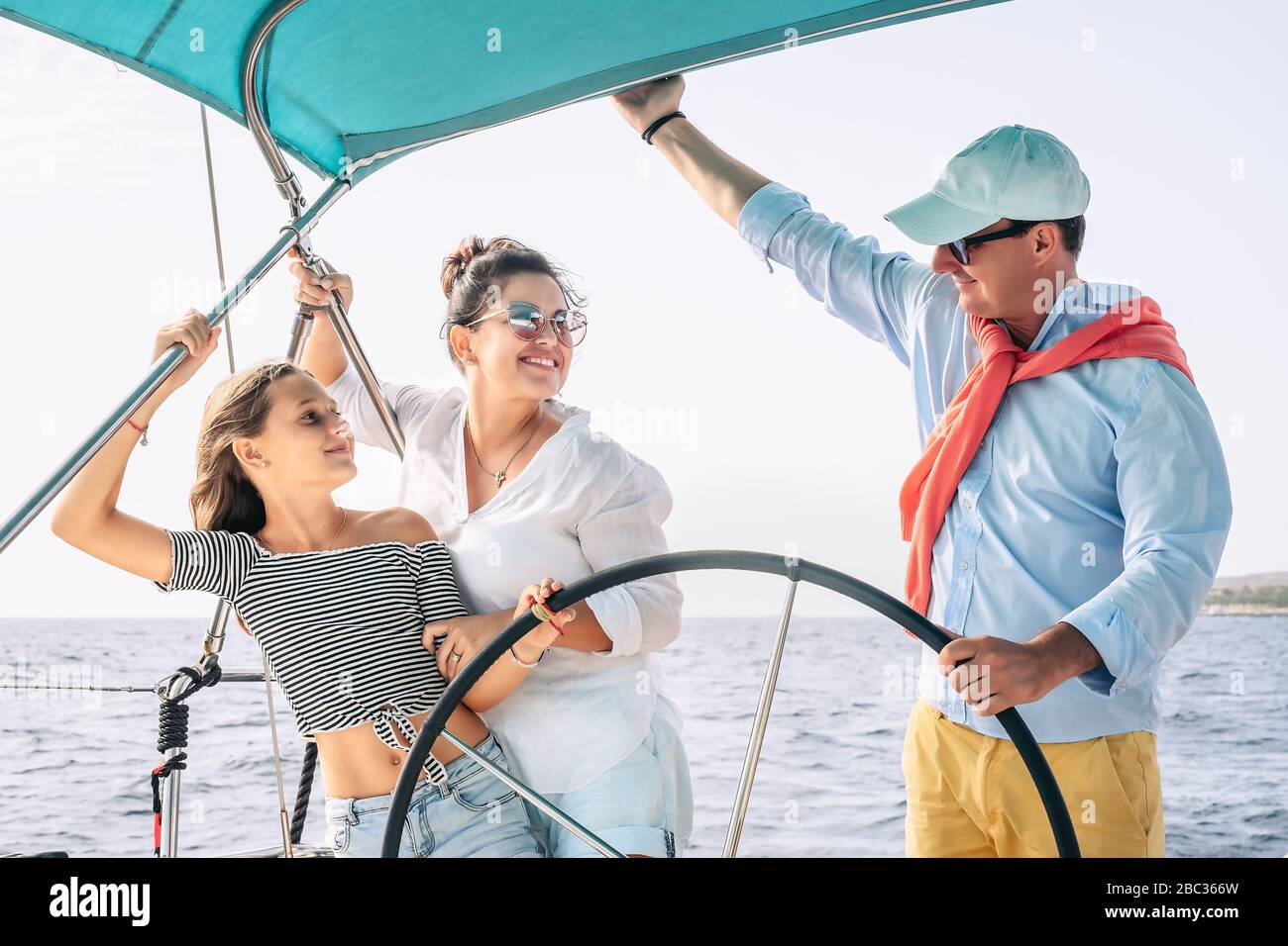 Happy family having fun on sailboat vacation - Mother father and daughter enjoying time together doing luxury boat trip Stock Photo