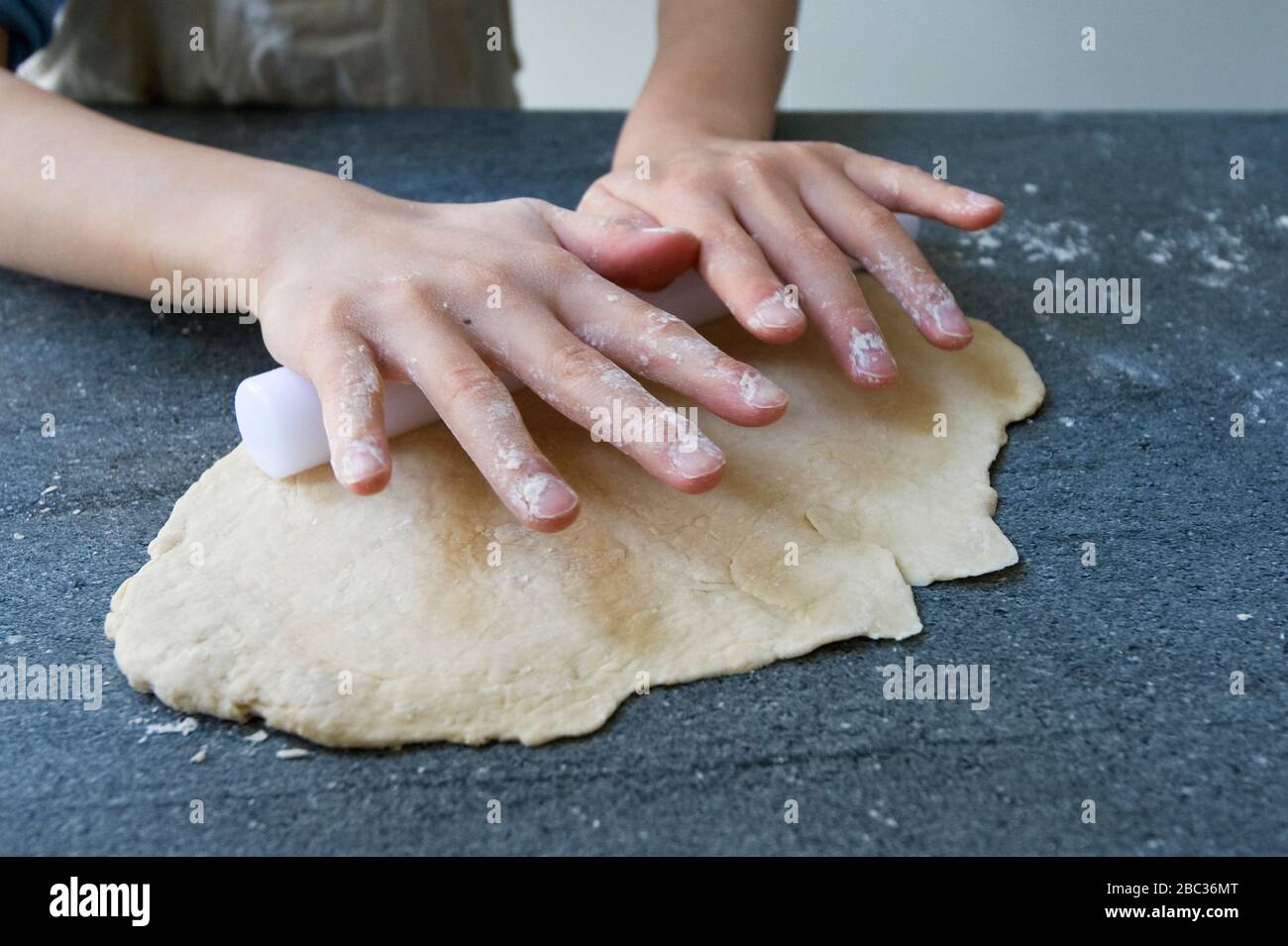Child using plastic rolling pin to flatten out dough to make pizza or pastry. Stock Photo
