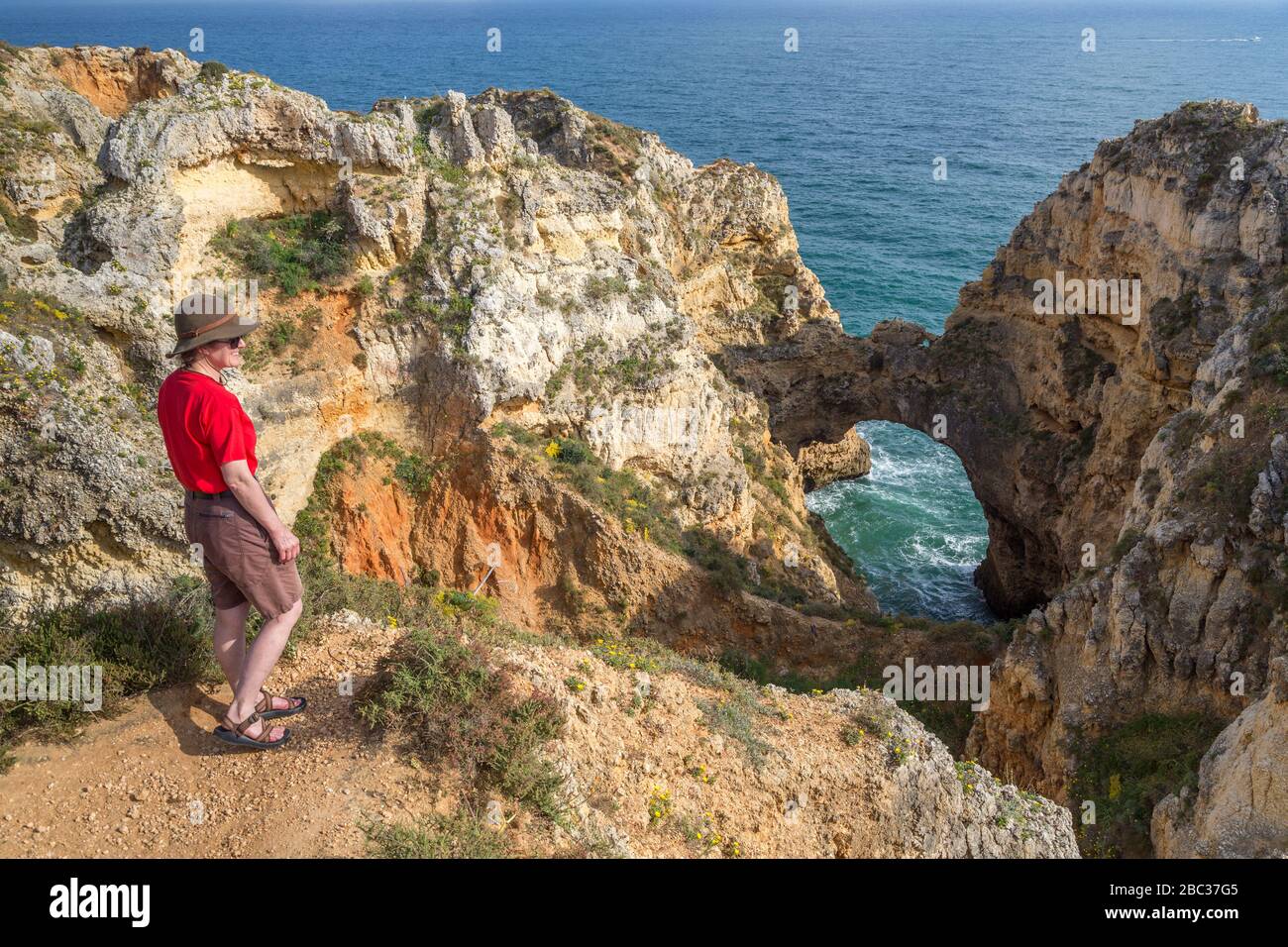 Woman standing on cliff edge near sea arch, Pont Piedade, Algarve, Porgugal Stock Photo