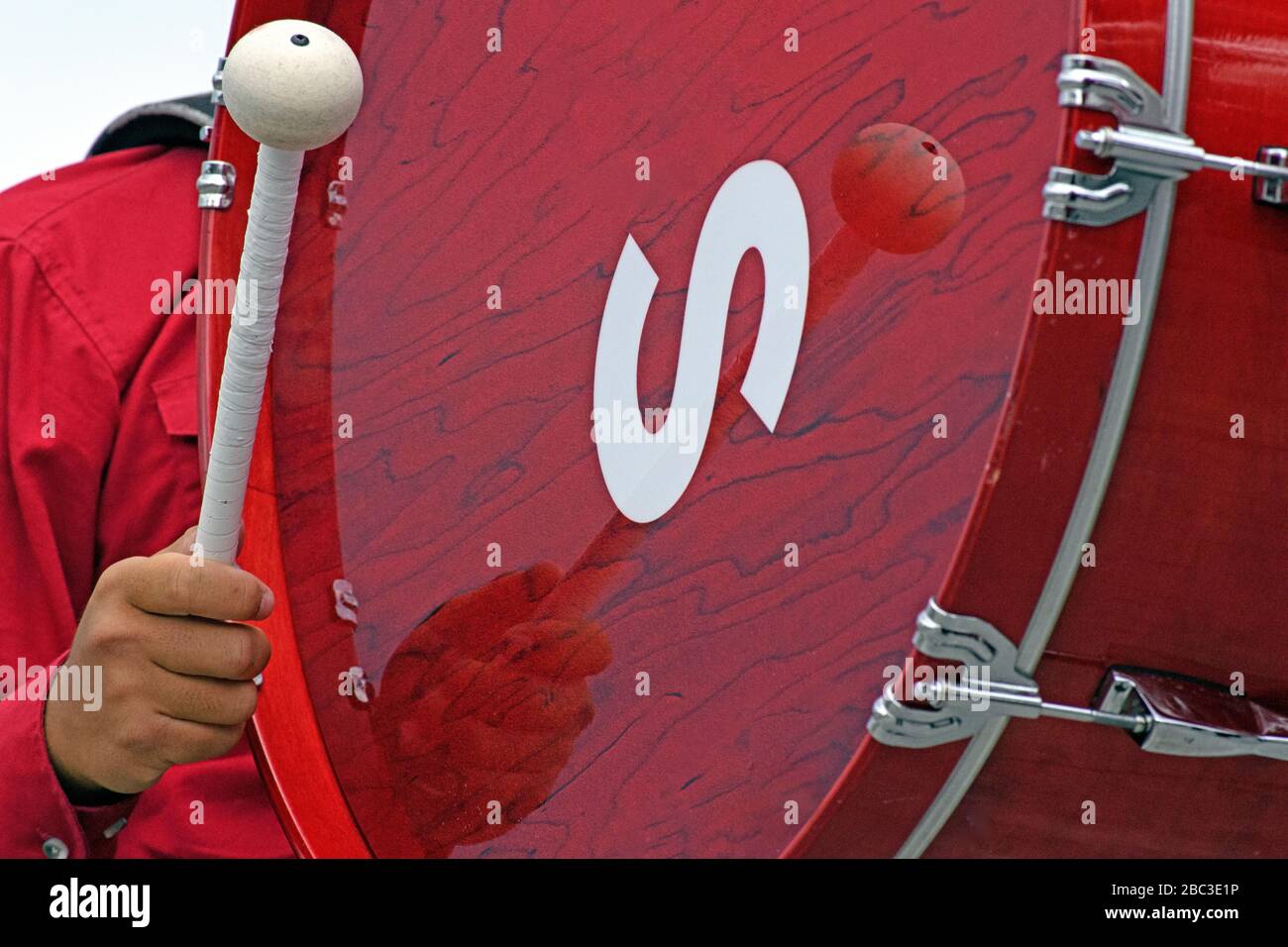 Musical band member playing a large red bass drum during an outdoor
