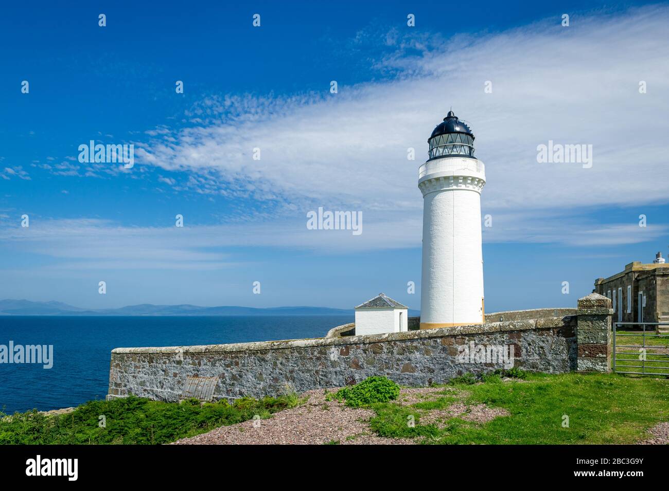 White lighthouse tower and stone fence. Davaar island, Scotland Stock Photo