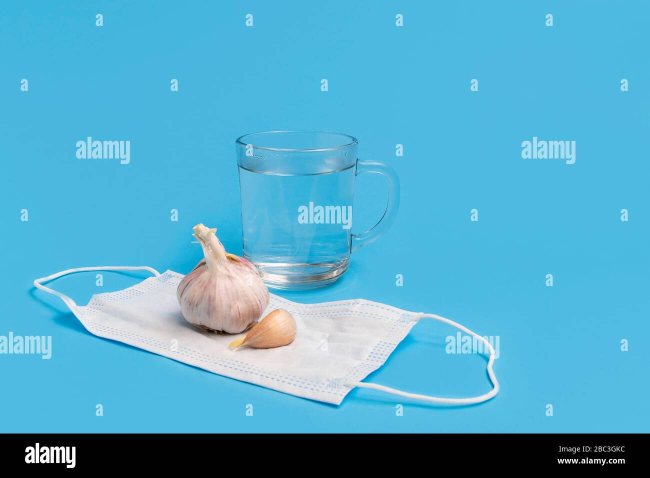 Coronavirus health myths concept, garlic, hot water, medical face mask on blue background with copy space Stock Photo