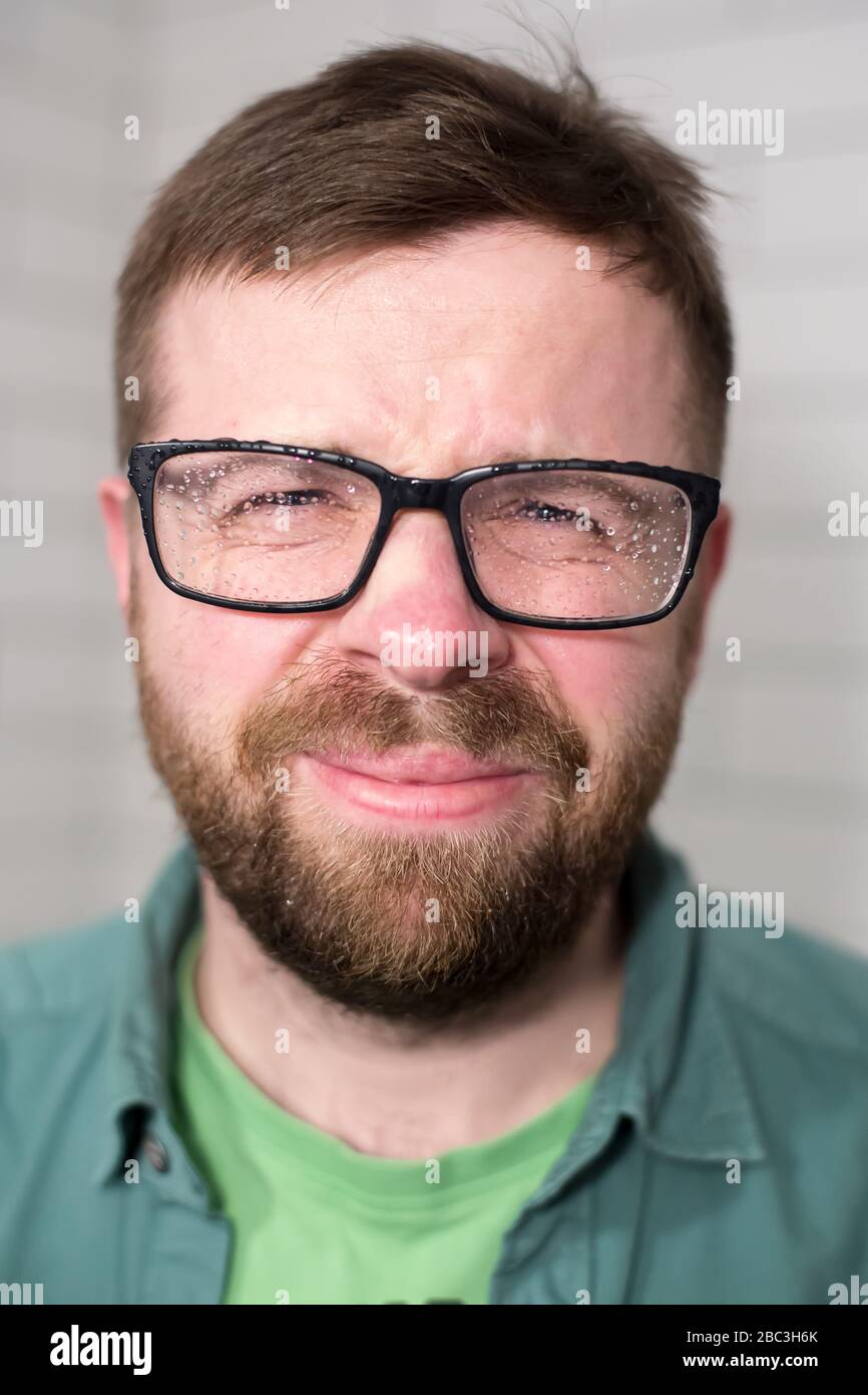 Attractive bearded man in glasses with raindrops, he feels discomfort due to wet lenses. Stock Photo