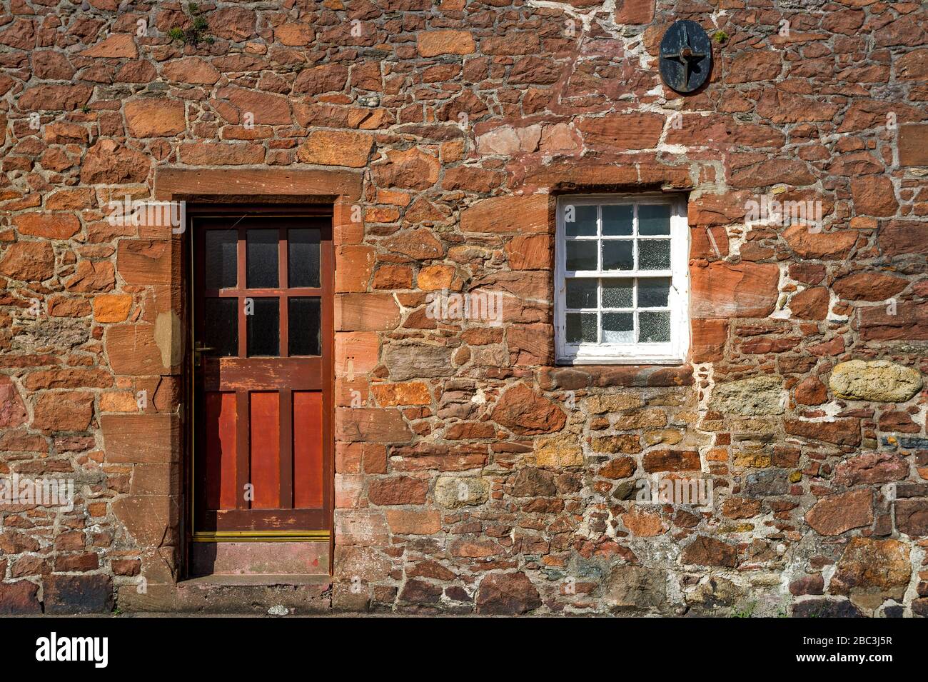 Red medieval wall with wooden door and fortified window. Campbeltown street, Scotland. Stock Photo