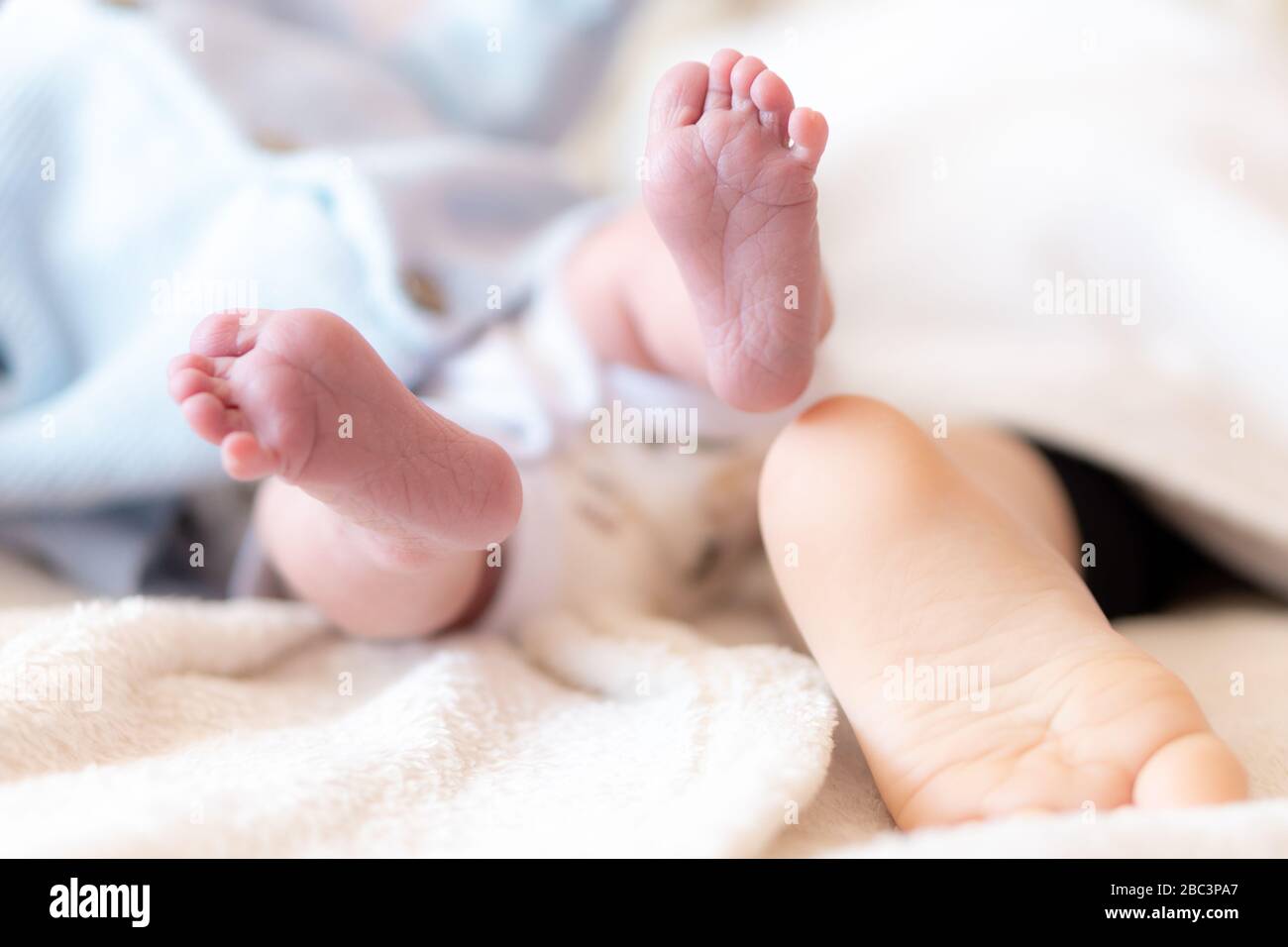 Close-up of the foot of a newborn baby and a one-year-old baby. Feet of infants of different ages sleeping. Foot of a newborn over the foot of another Stock Photo
