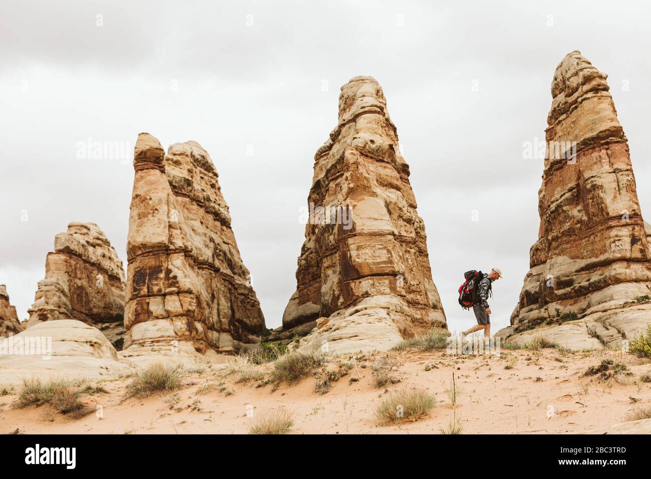 Hiker with backpack walks next to red sandstone towers in utah desert Stock Photo