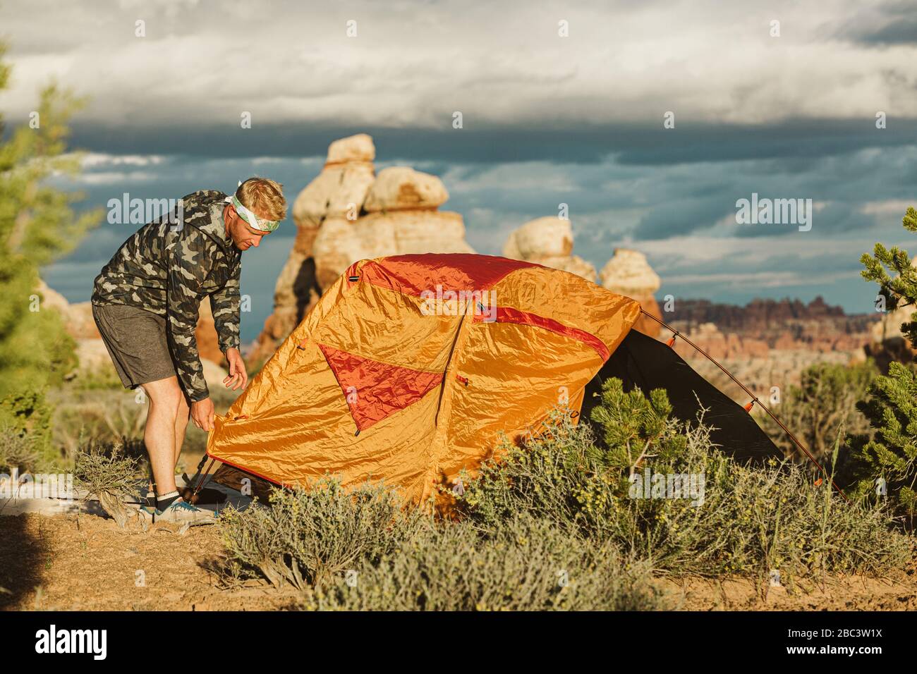 camper in camo windbreaker finishes setting up tent in utah desert Stock Photo