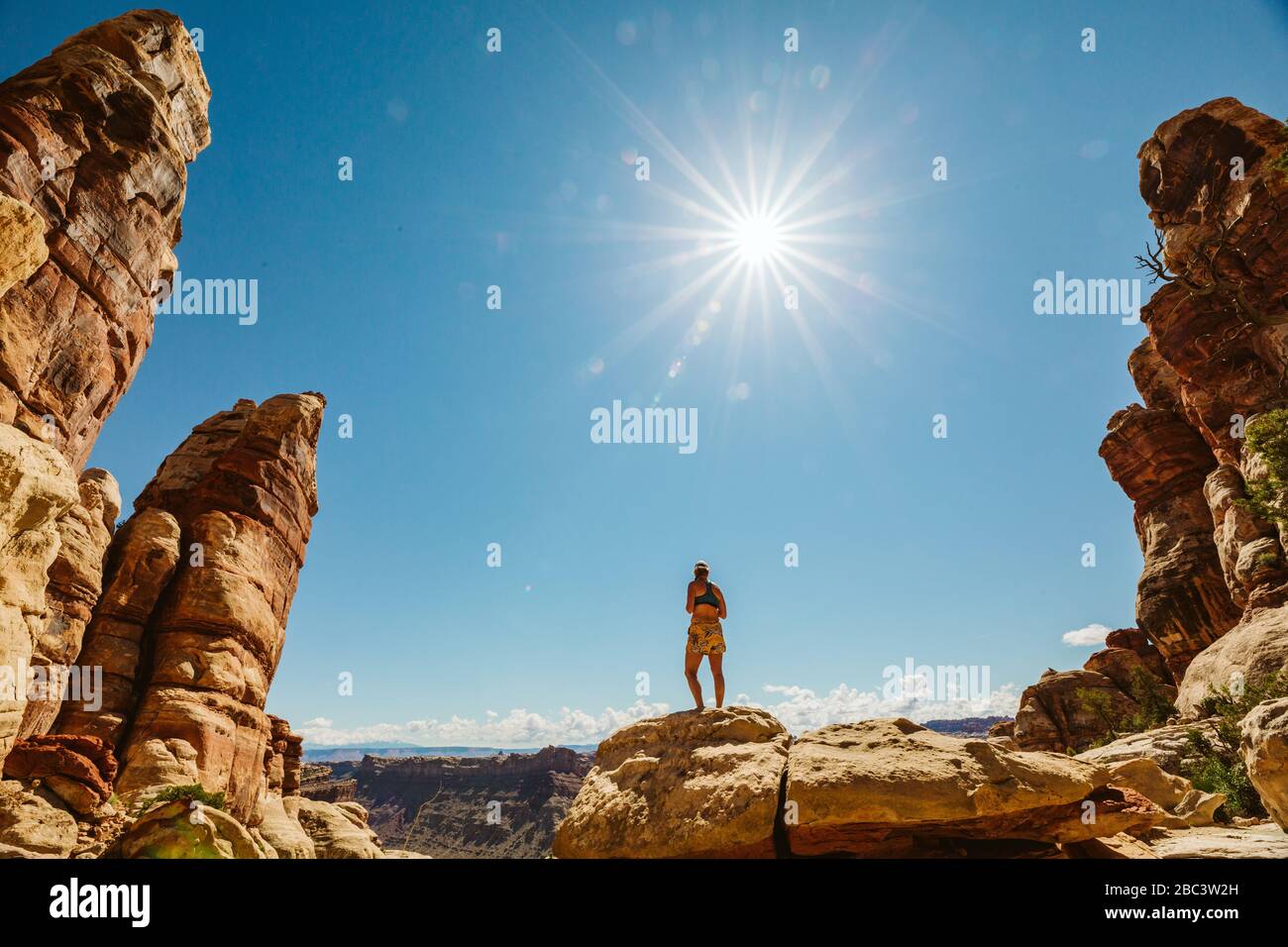 woman in sports bra and shorts stands on rocks in desert under sun Stock Photo