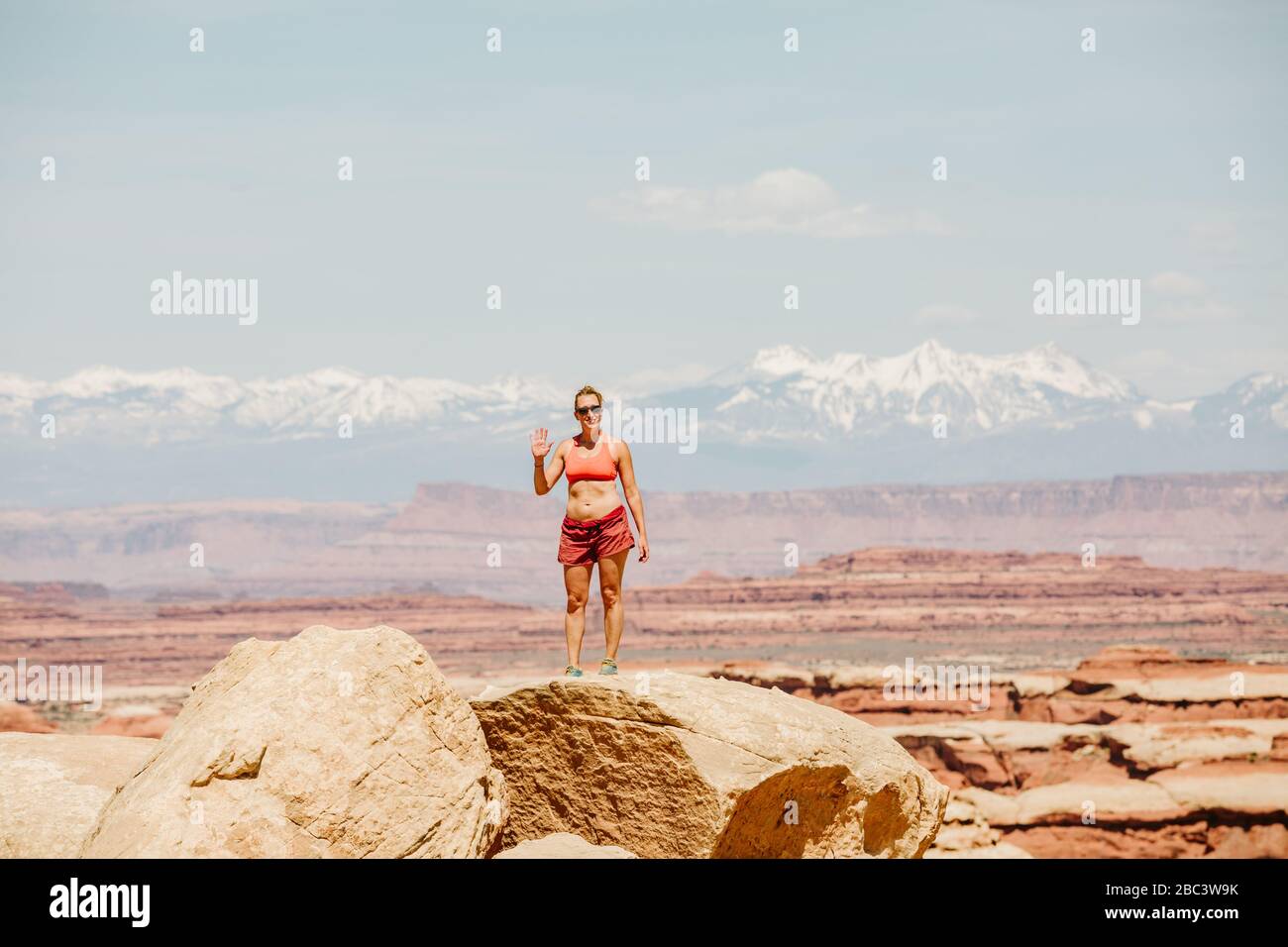 female hiker in sports bra and shorts waves from a desert