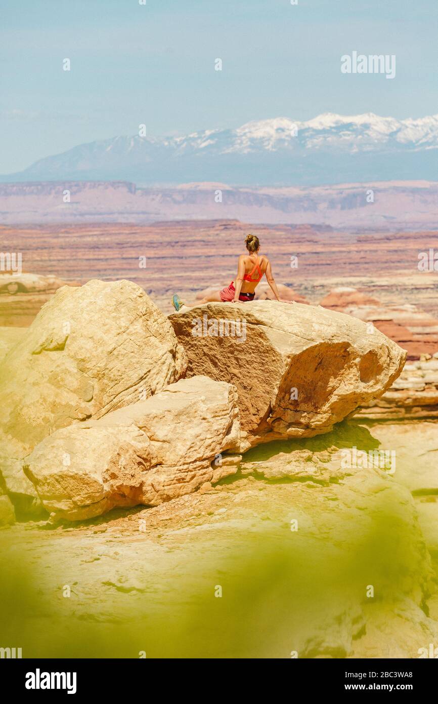 female hiker in sports bra rests on large rock overlooking canyonlands Stock Photo