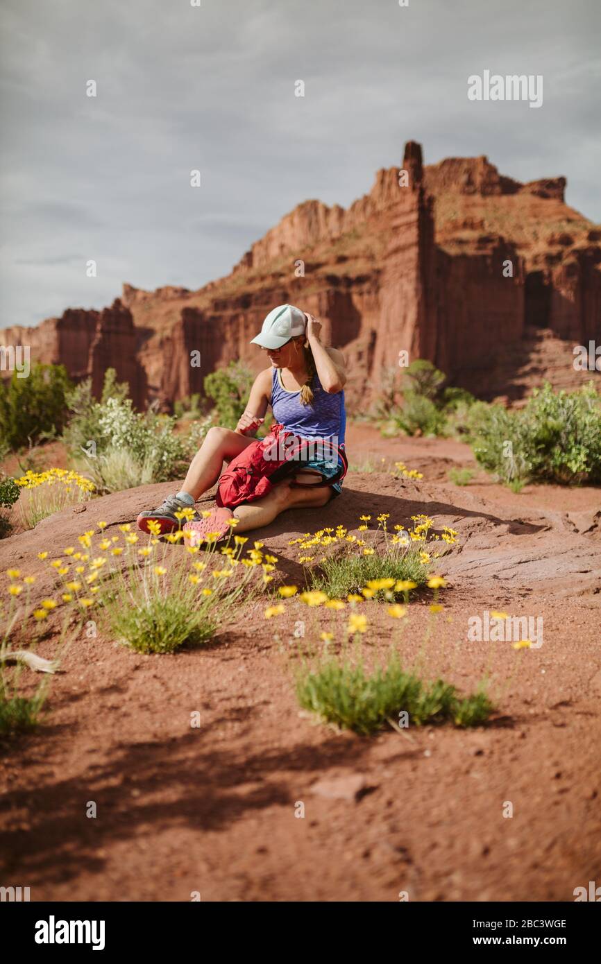 woman hiker adjust her hat while resting amongst yellow desert flowers Stock Photo