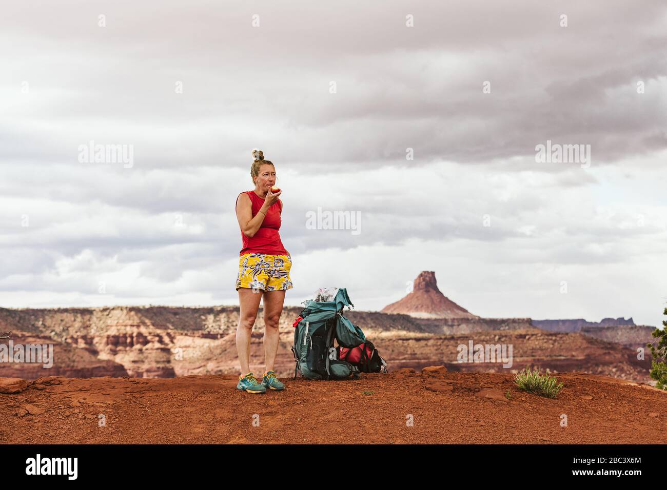 tired female hiker eats apple during a long day backpacking in desert Stock Photo