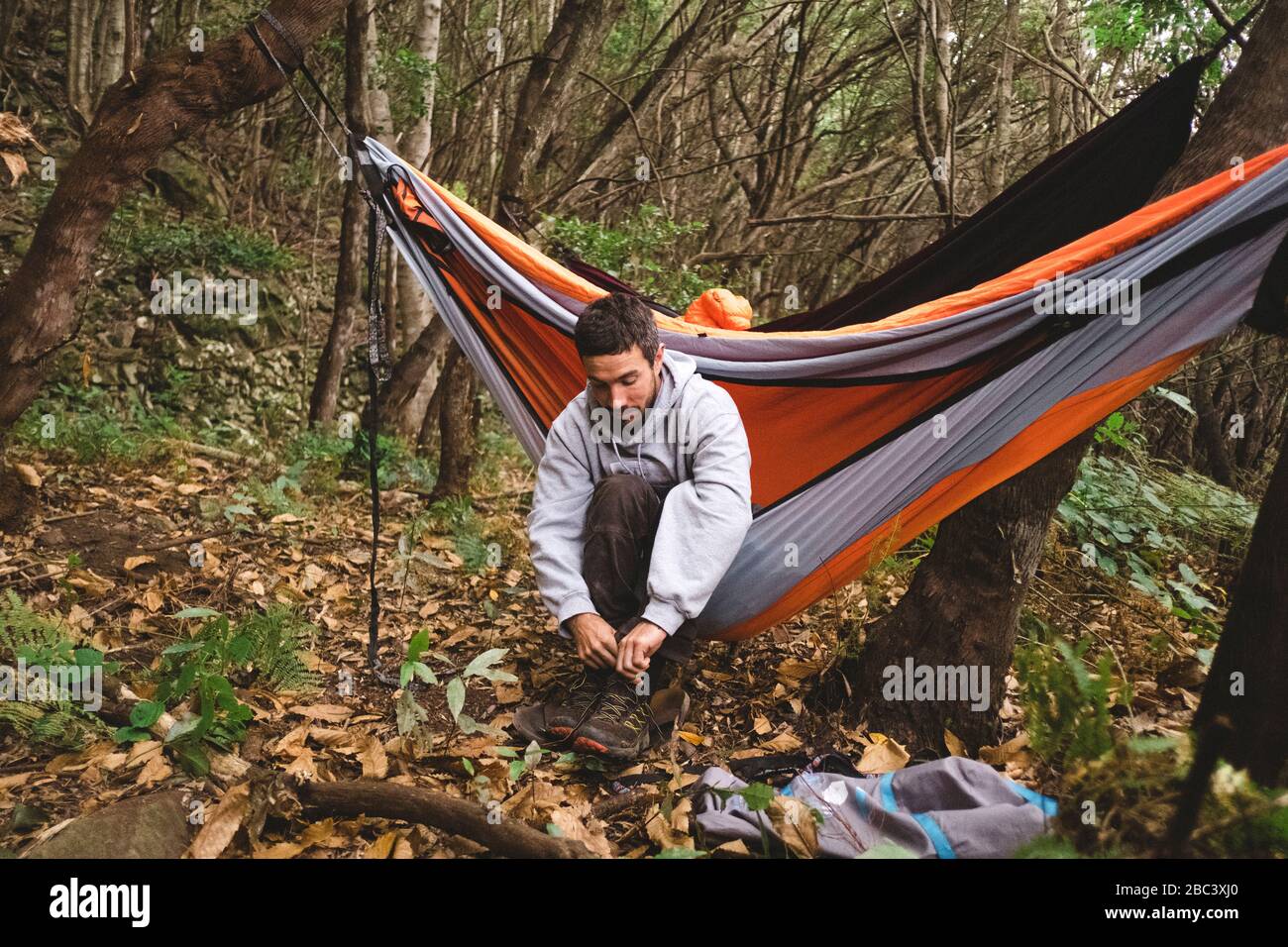 A man prepares for a hike sitting in a hammock in the forest Stock Photo