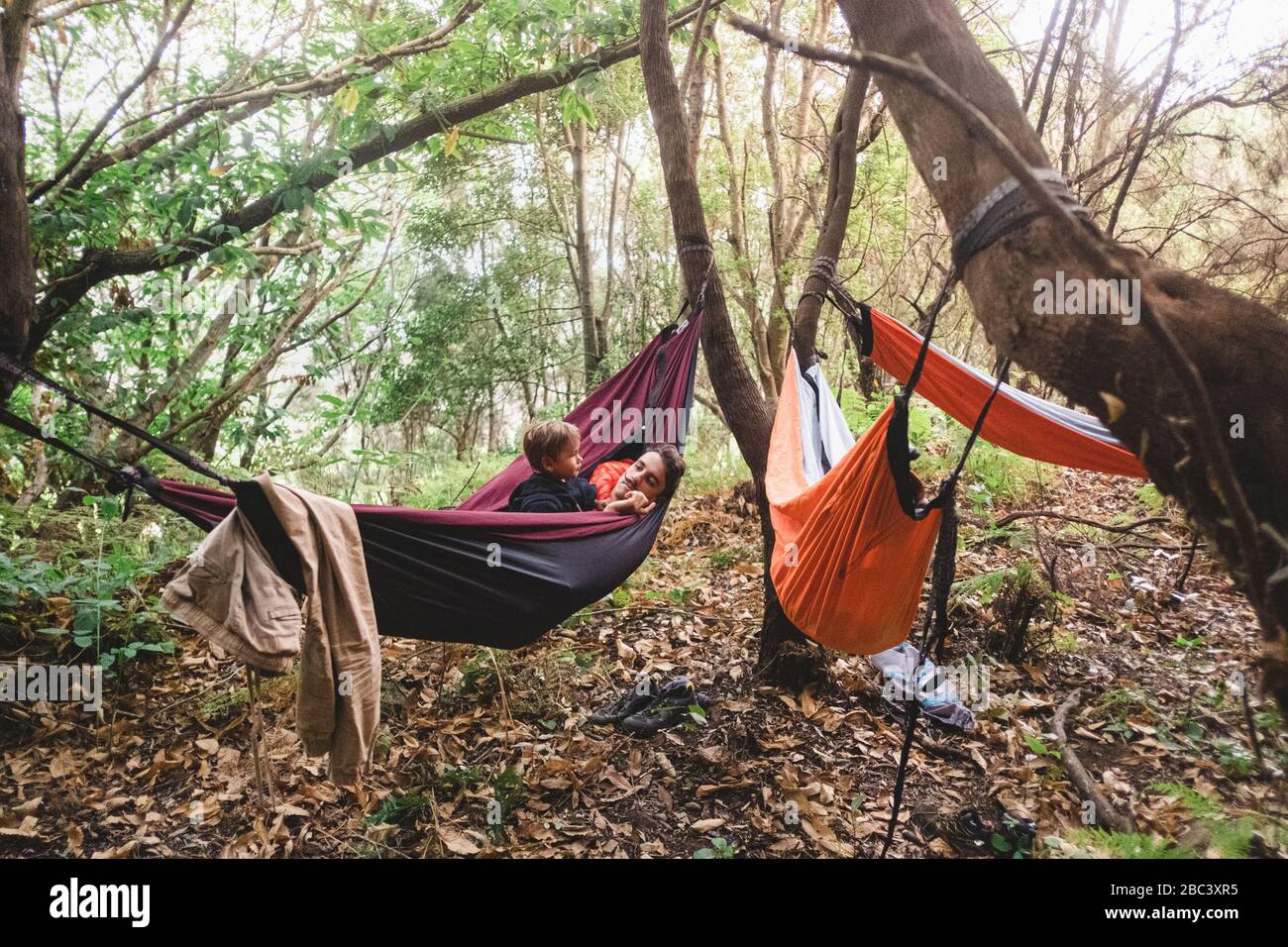 A man and young kid lying in a hammock in the forest Stock Photo
