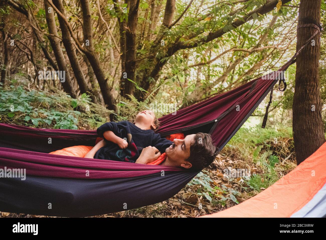 A man and a young kid lying in a hammock in the forest Stock Photo