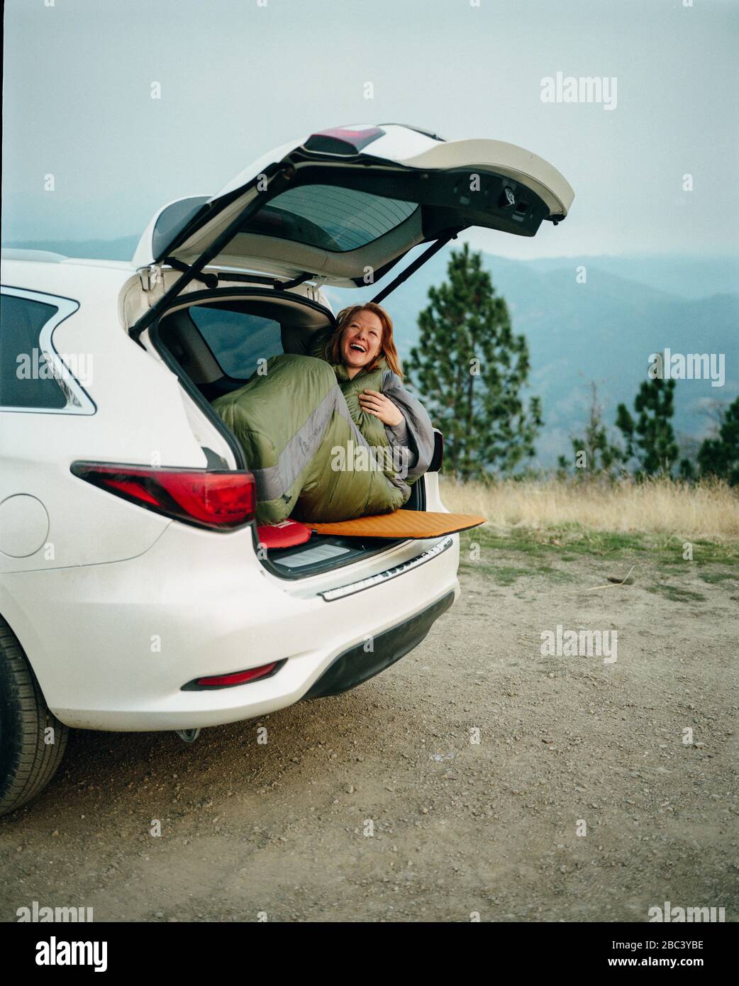 Woman in sleeping bag laughing while car camping in Big Sur Stock Photo