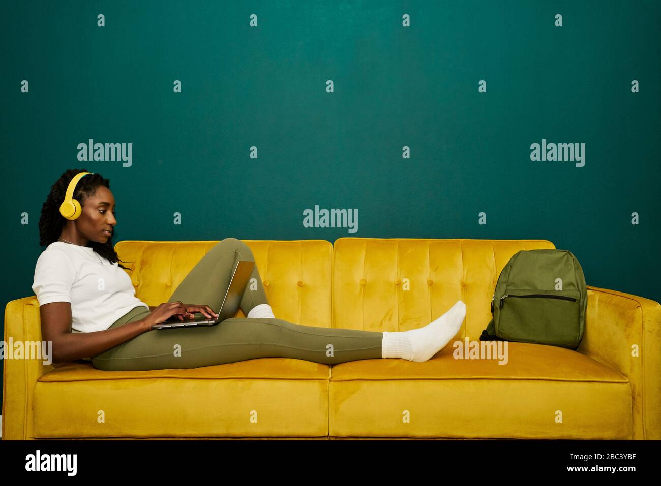 Afroamerican student laying at a yellow sofa front a dark green wall Stock Photo