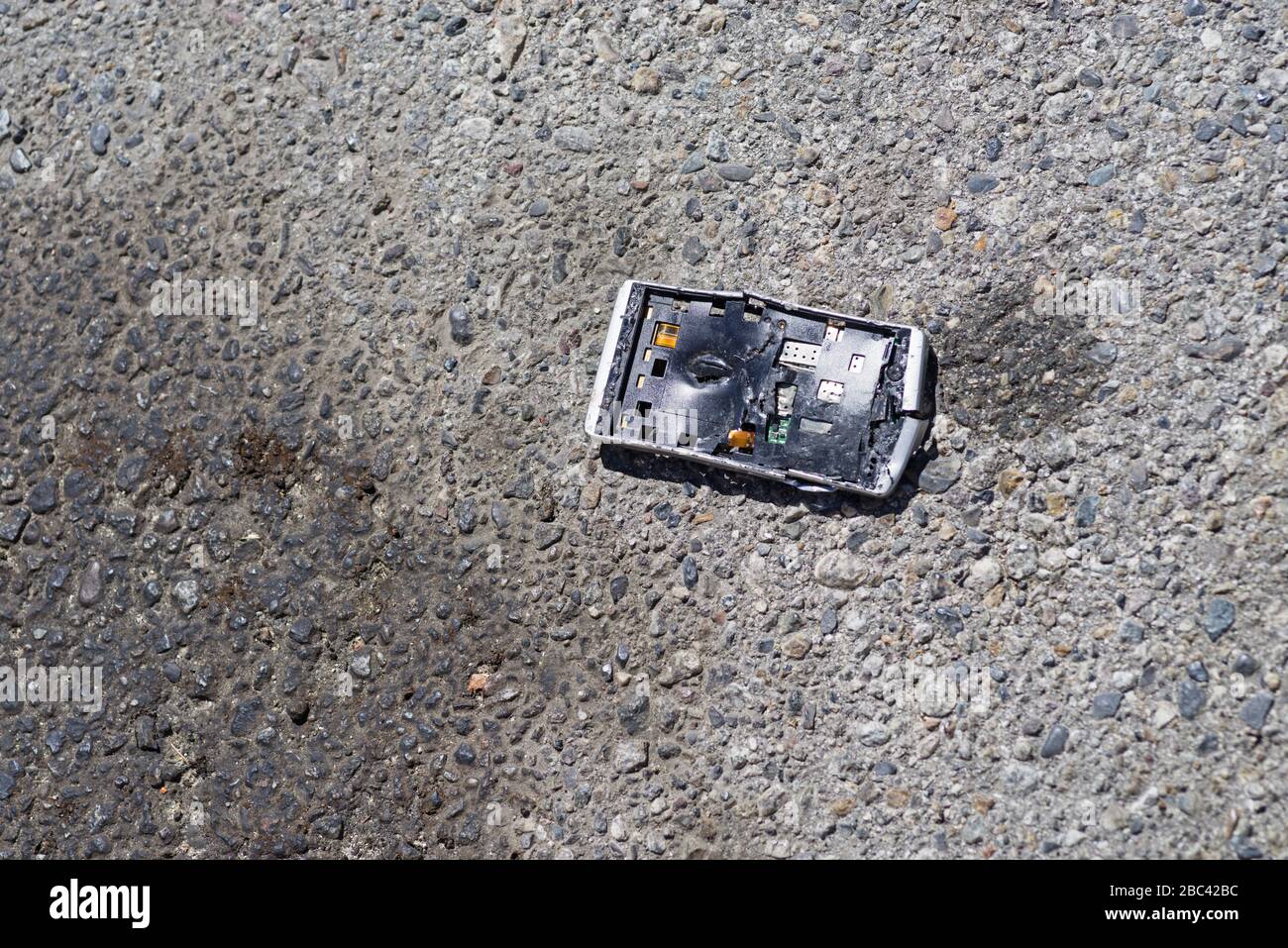 a smashed apart broken cell phone on the pavement of a road Stock Photo