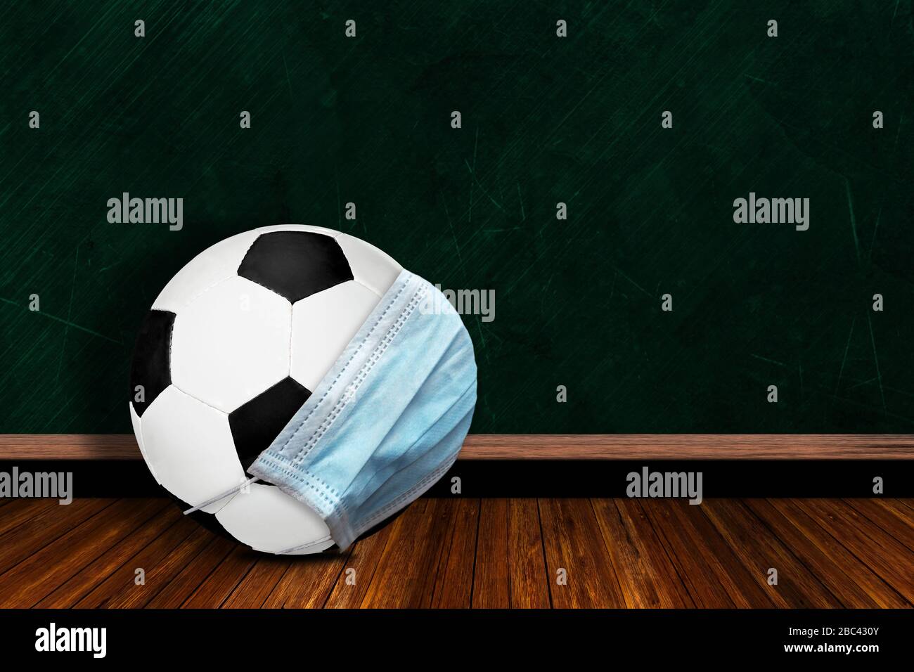 Soccer ball wearing surgical mask on a background chalk board with copy space for text. Concept of COVID-19 coronavirus pandemic affecting football or Stock Photo