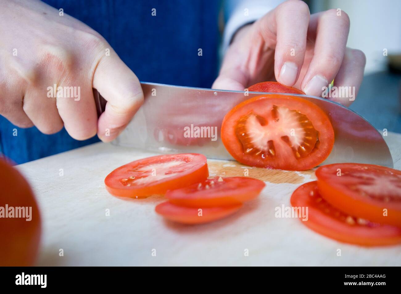 A pair of hands holding a sharp knife to slice a tomato into slices