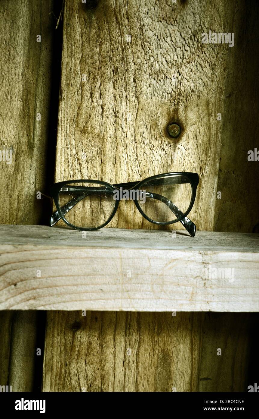 A pair of black specs  spectacles sitting on a wooden ledge of a wooden hut. Stock Photo
