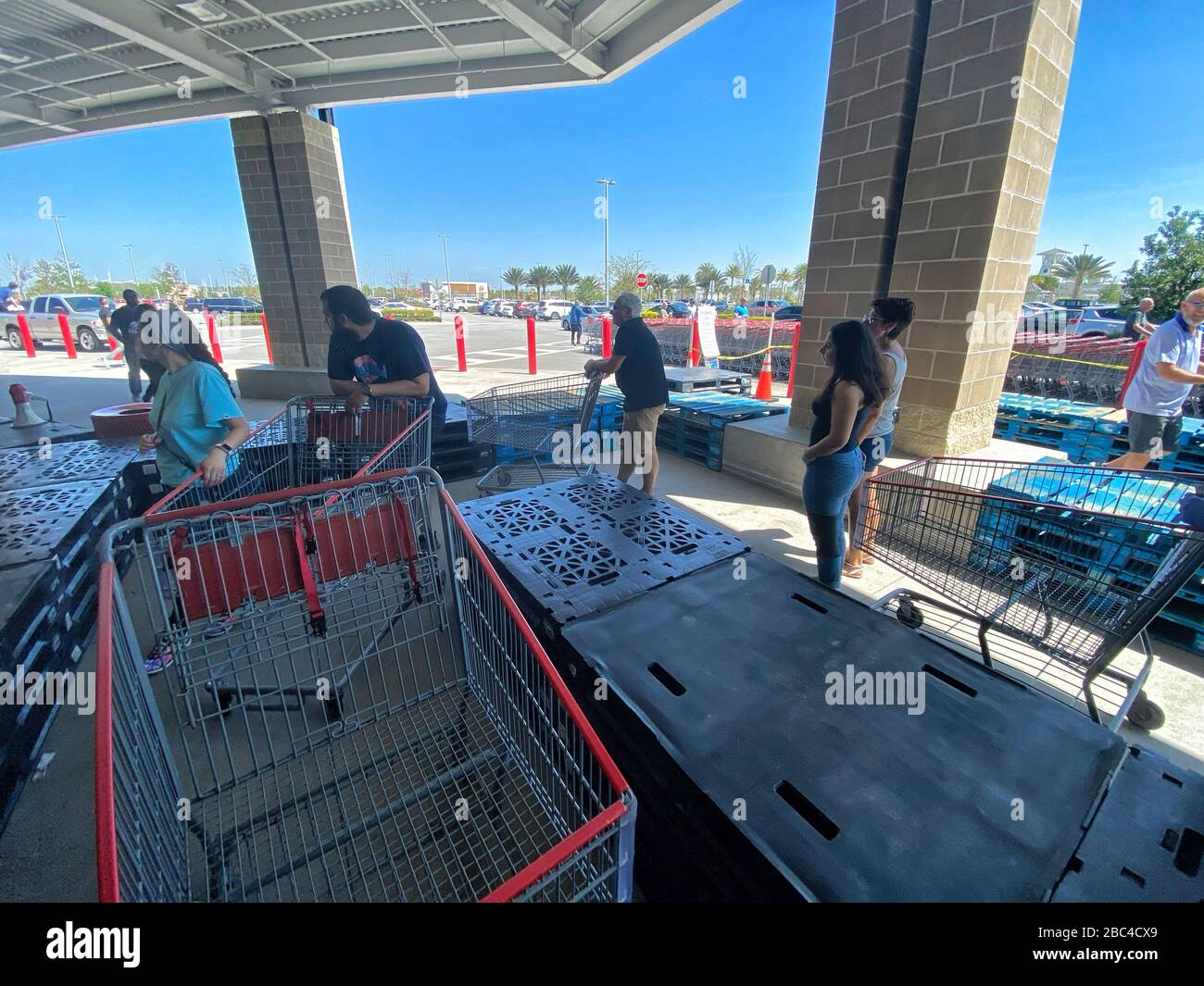 Shoppers line up at Costco maintaining social distancing. Wooden palettes have been placed to help people keep apart and form a line with enough space between each other. Stock Photo