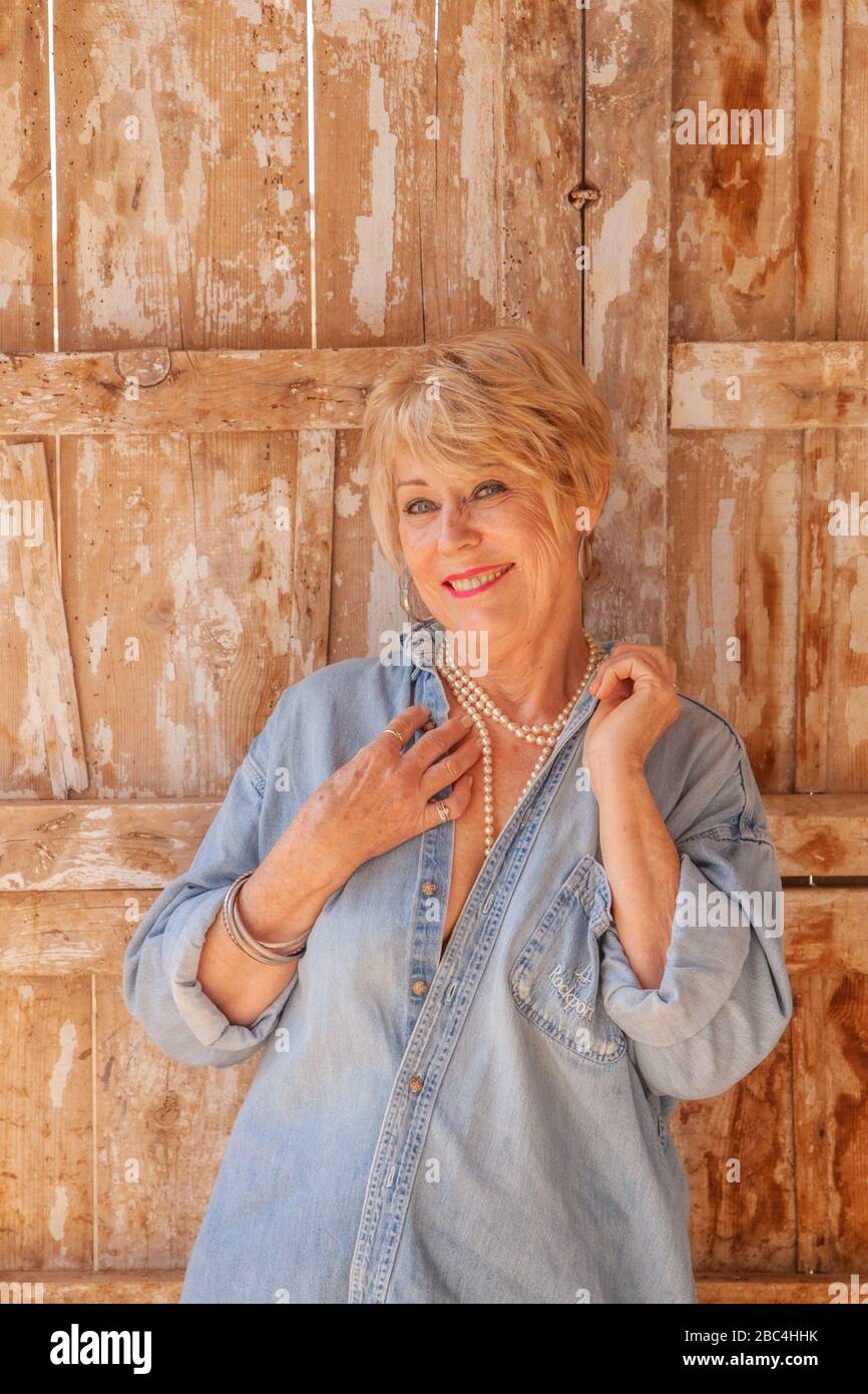 Attractive mature woman posing in her derelict spanish barn, wearing pearls and a denim shirt Stock Photo