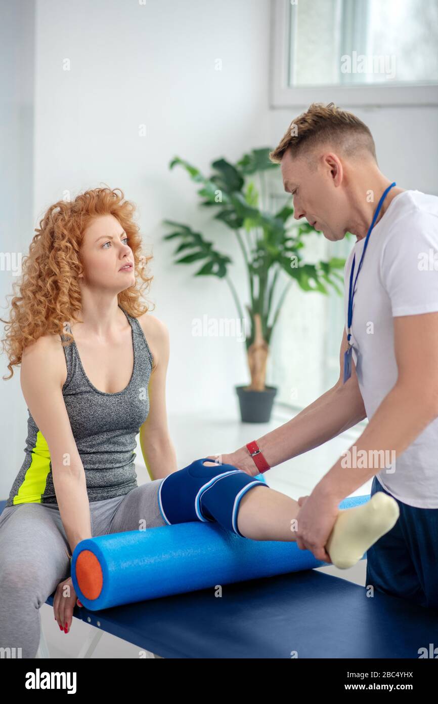 Male physiotherapist examining knee bandage of female patient sitting